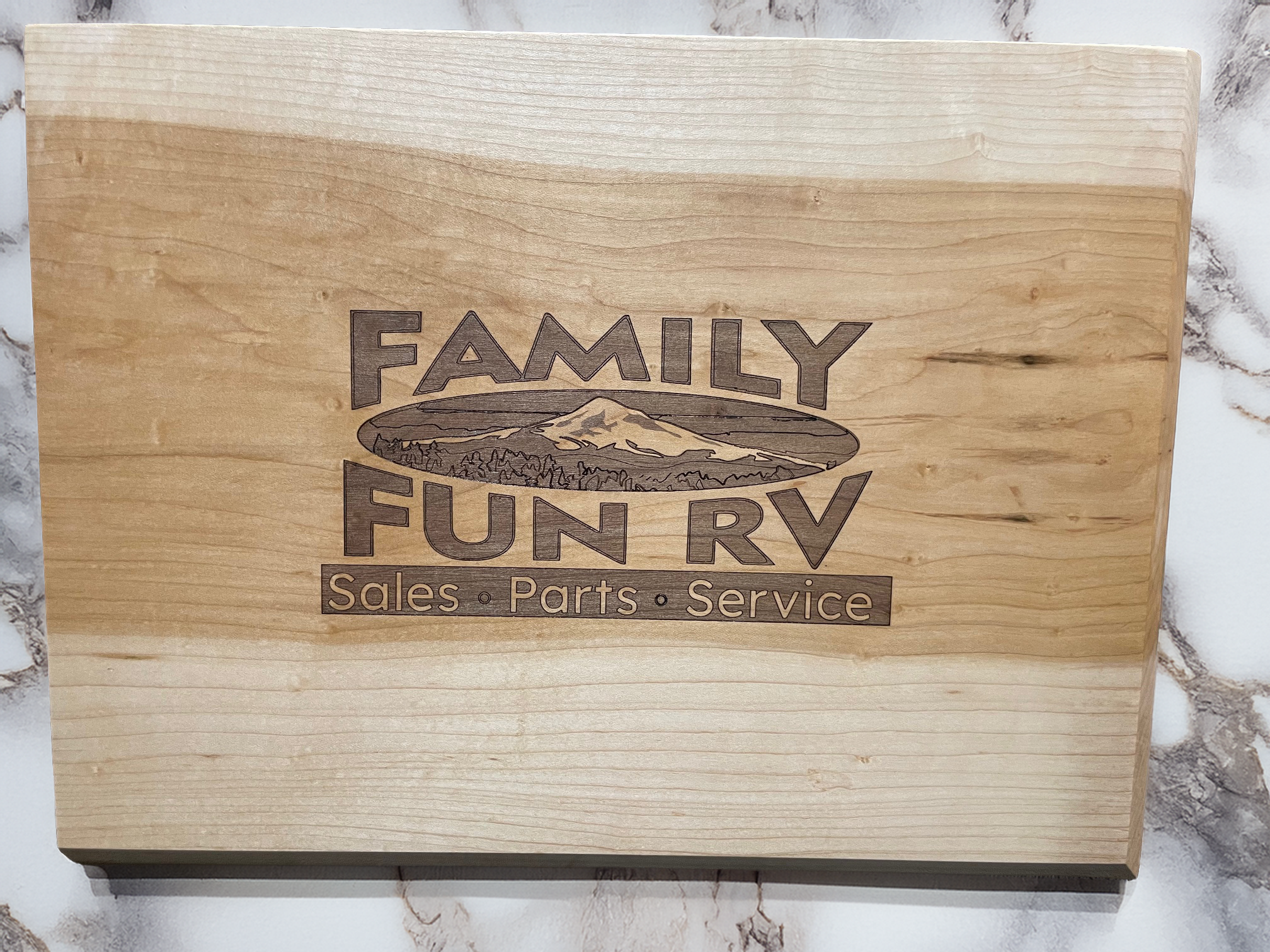 A wooden sign with the logo of Family Fun RV, featuring a mountain and forest scenery. Text reads "Family Fun RV" with additional words "Sales, Parts, Service" underneath.