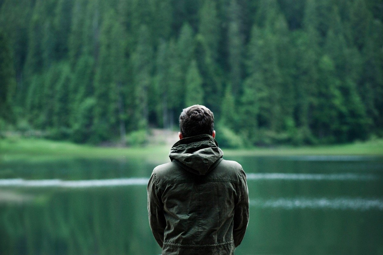 man looking out over water into a forest