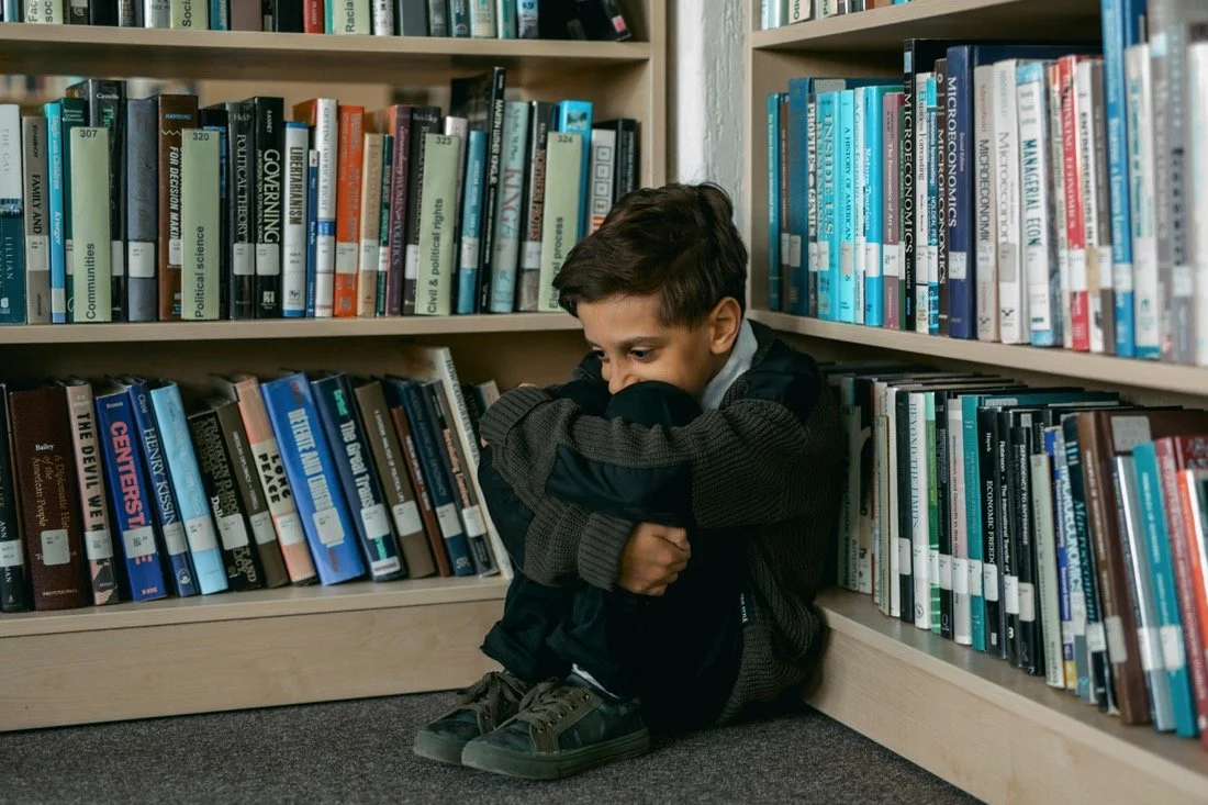 A litle boy sitting all hunched up in a library