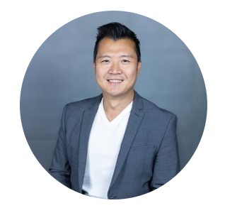 Headshot of a smiling man in a gray blazer and white shirt against a blue background.