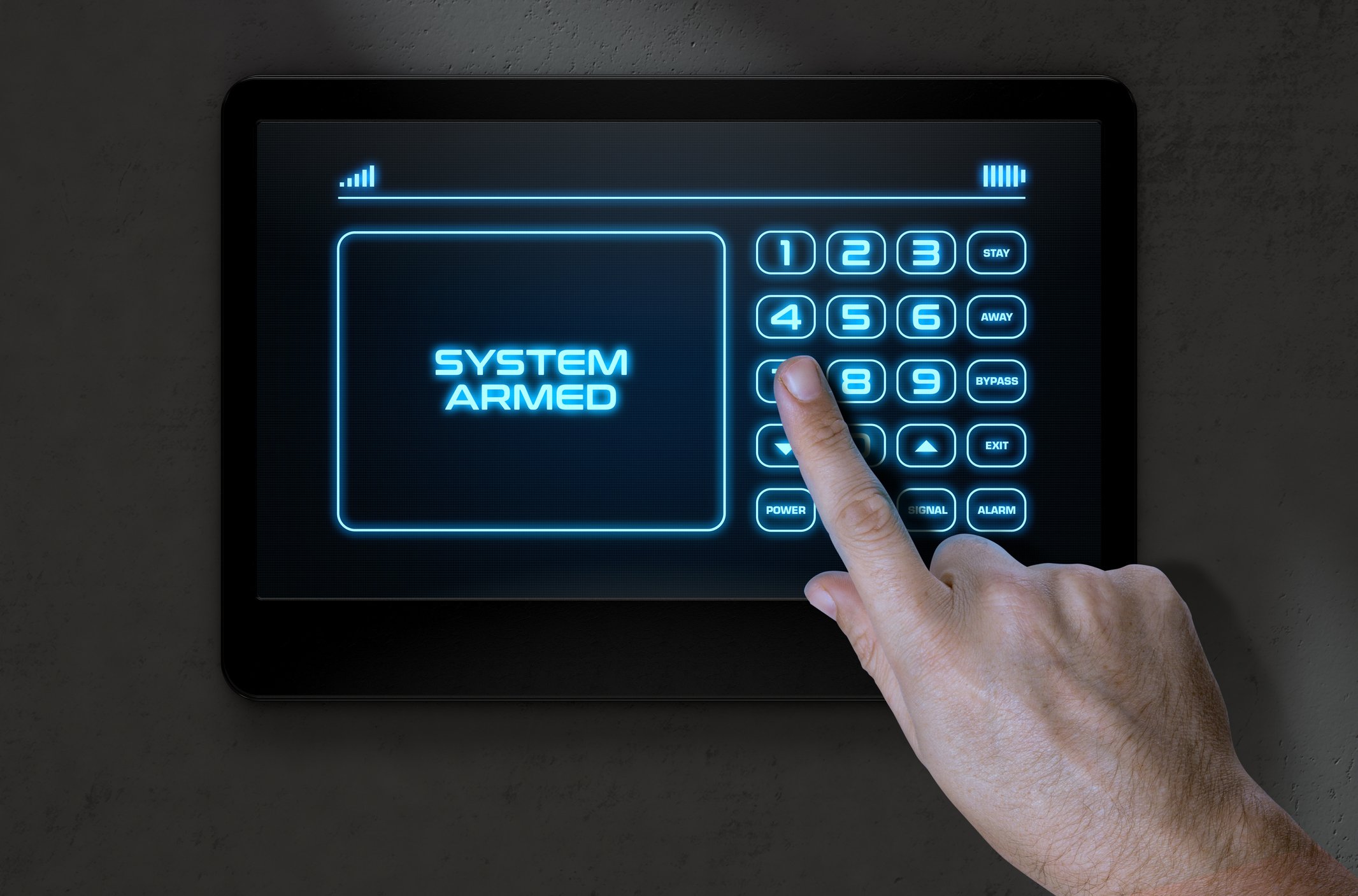 A person presses a button on an electronic security panel with a digital display showing the message 'SYSTEM ARMED' and various control options.
