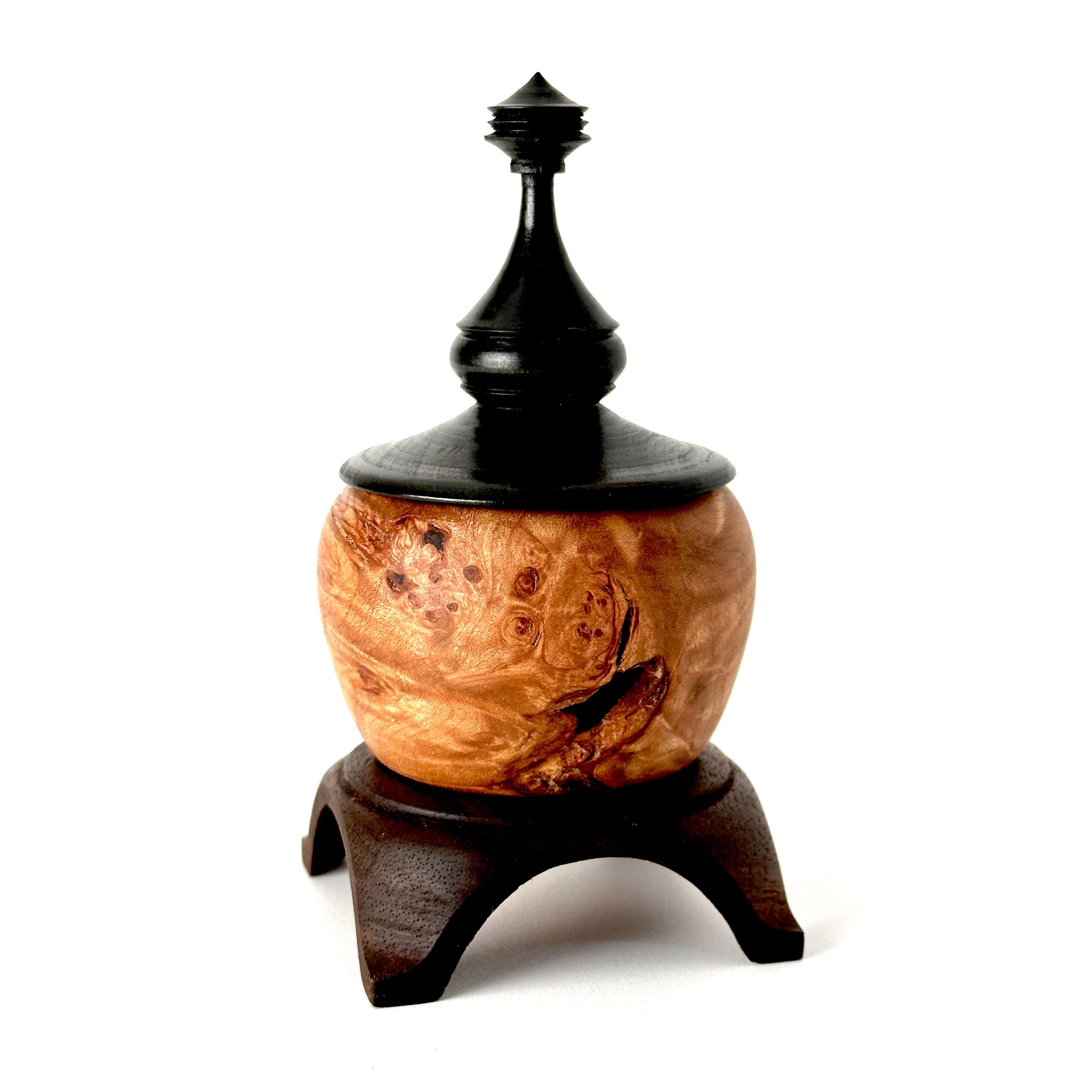 Decorative wooden and black carved container with a lid and stand, featuring a burl wood pattern on the body.