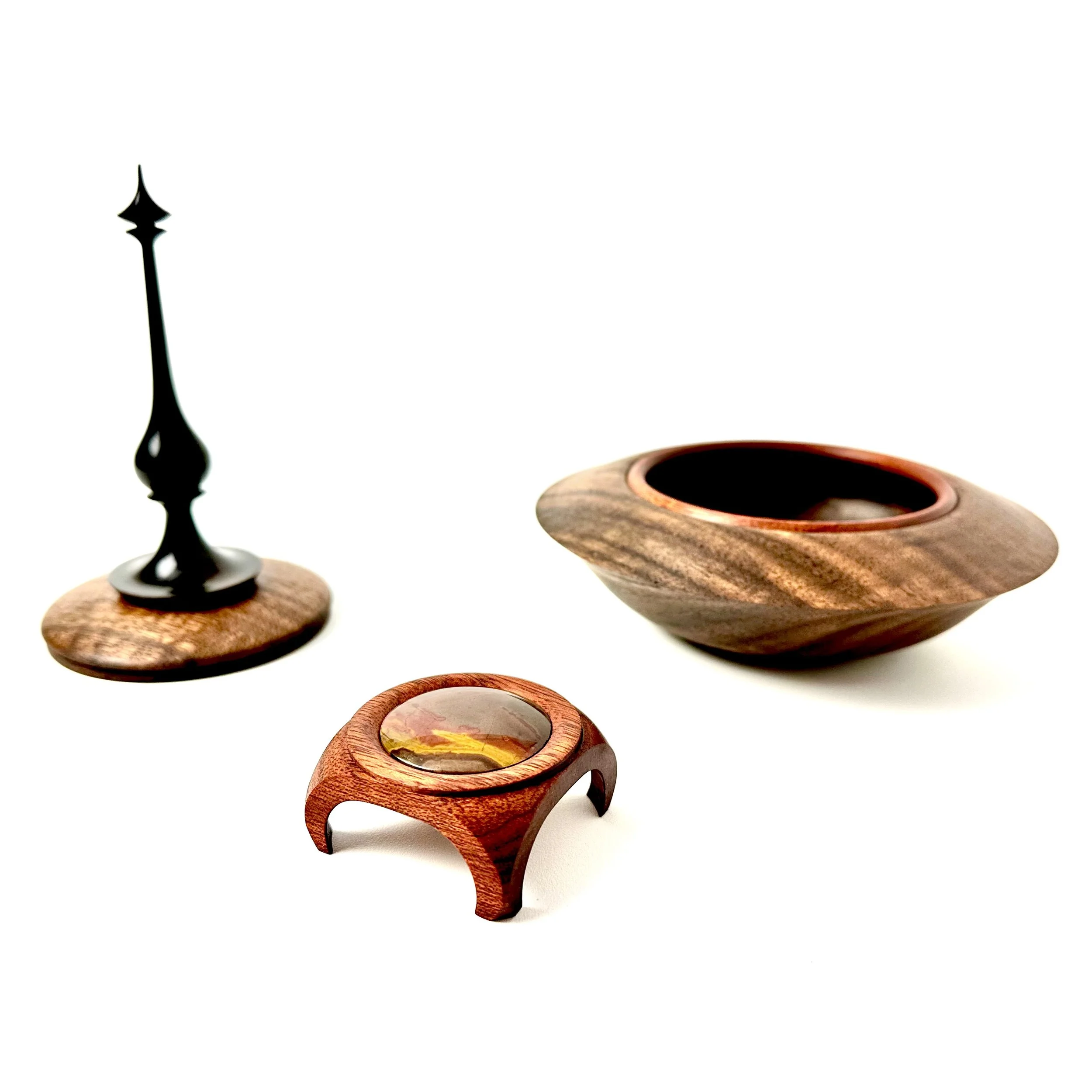 Three handcrafted wooden items: a tall black metal-tipped candle on a round wooden base, a shallow wooden bowl with a protruding lip, and a small wooden ring with a glass dome on top.
