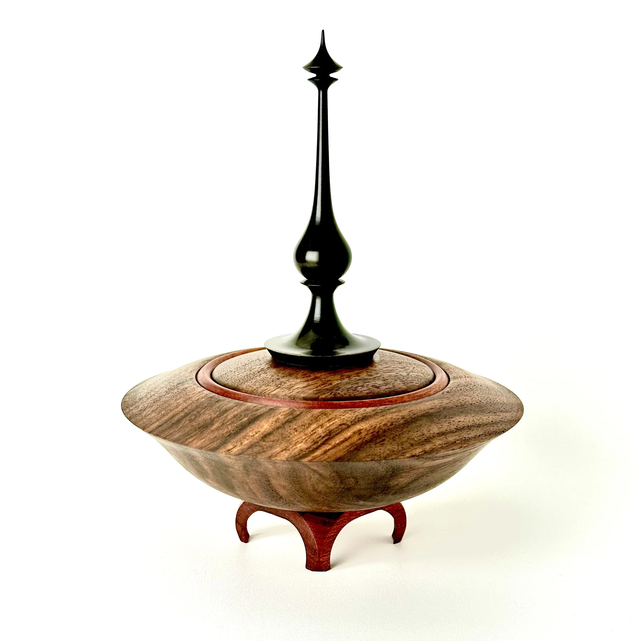 A decorative wooden spinning top with a black finial on top, set against a white background.