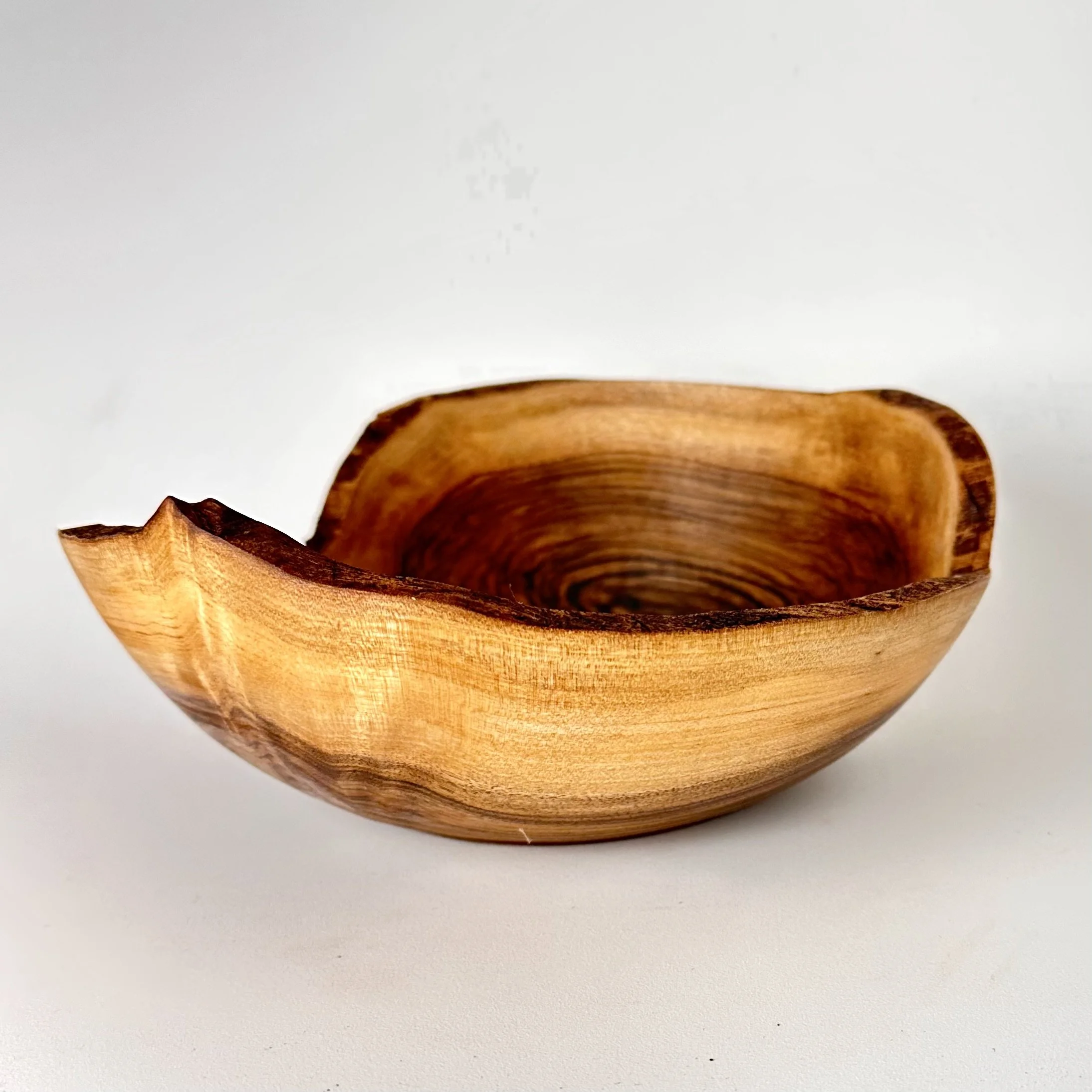 Wooden English walnut bowl with natural grain pattern and smooth natural live edge on a white background.