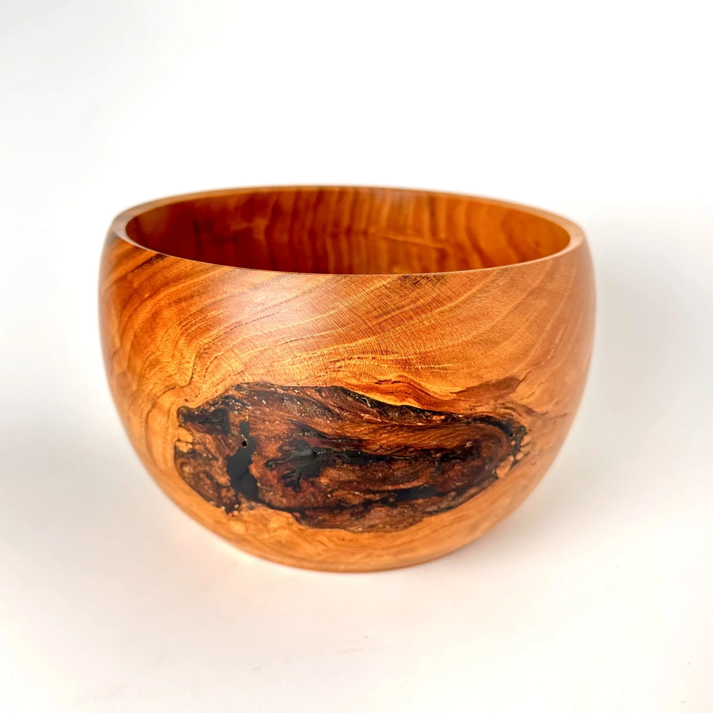 A polished bowl made from cherry wood with natural wood grain and a dark knot on one side, set against a plain white background.