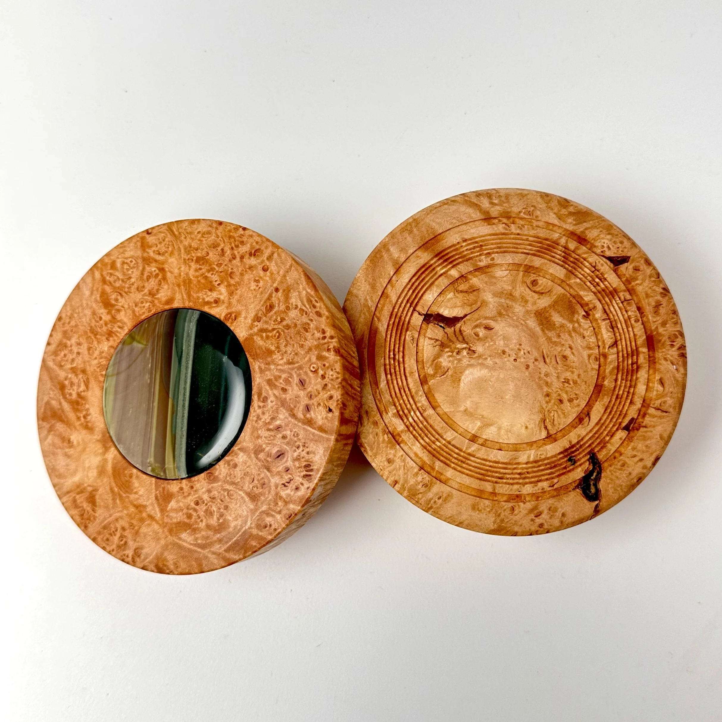 Two round wooden boxes with intricate patterns on their surfaces, the lid has an orbicular Blue Mountain Jasper with an ocean picture. 