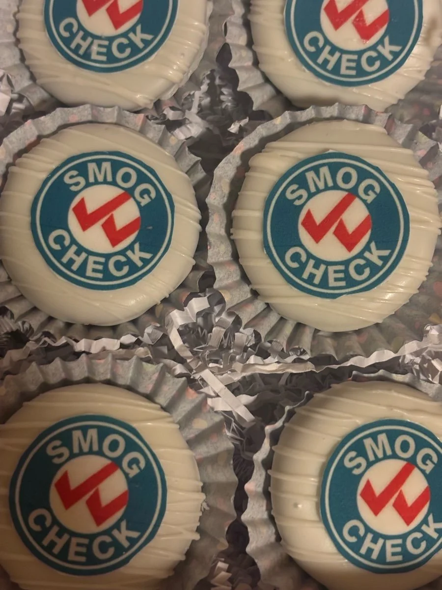 Six round white chocolates with a 'SMOG CHECK' logo on top, placed in metallic foil cups.