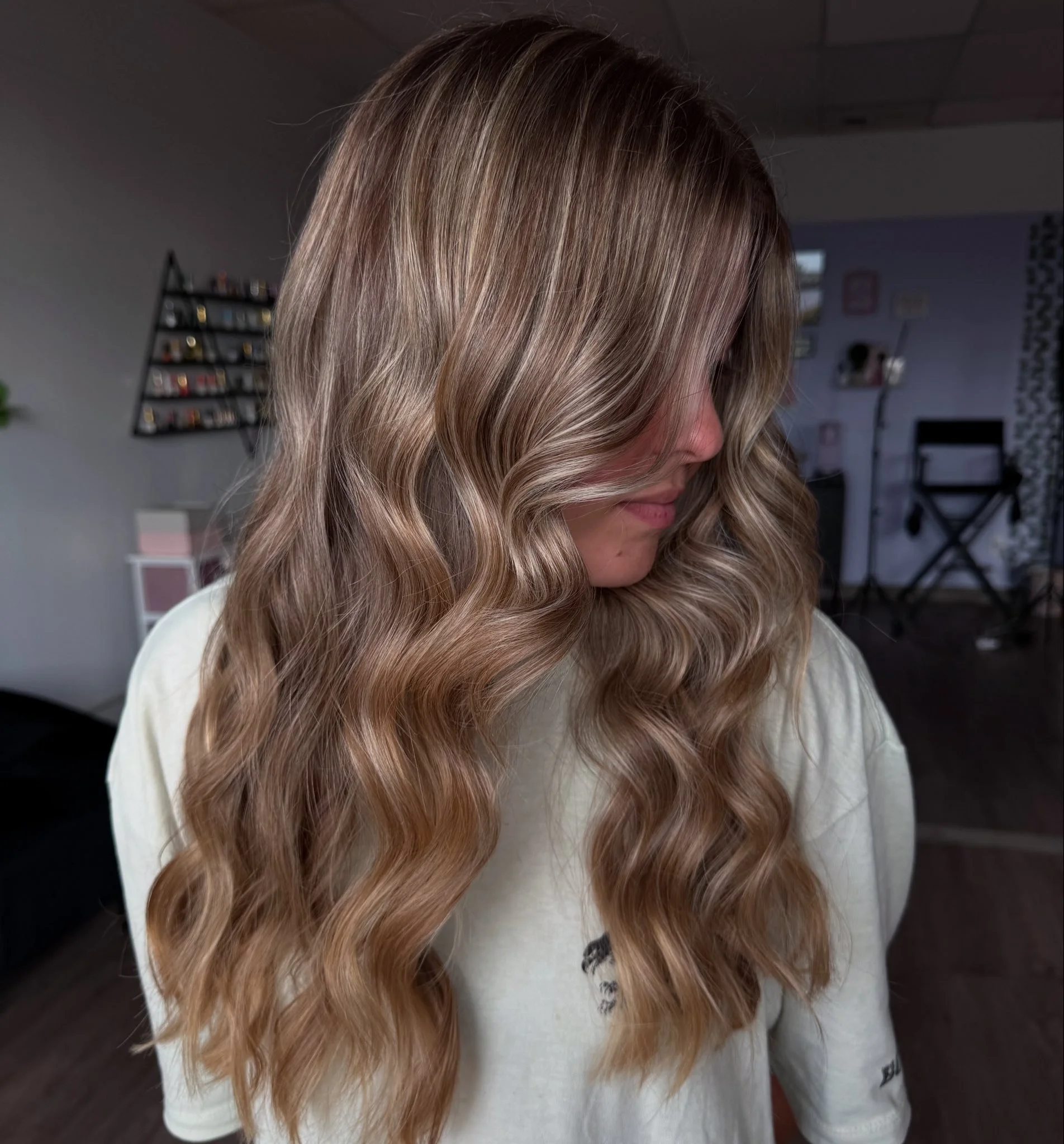 A woman with long, wavy blonde hair looking down in a hair salon or studio.