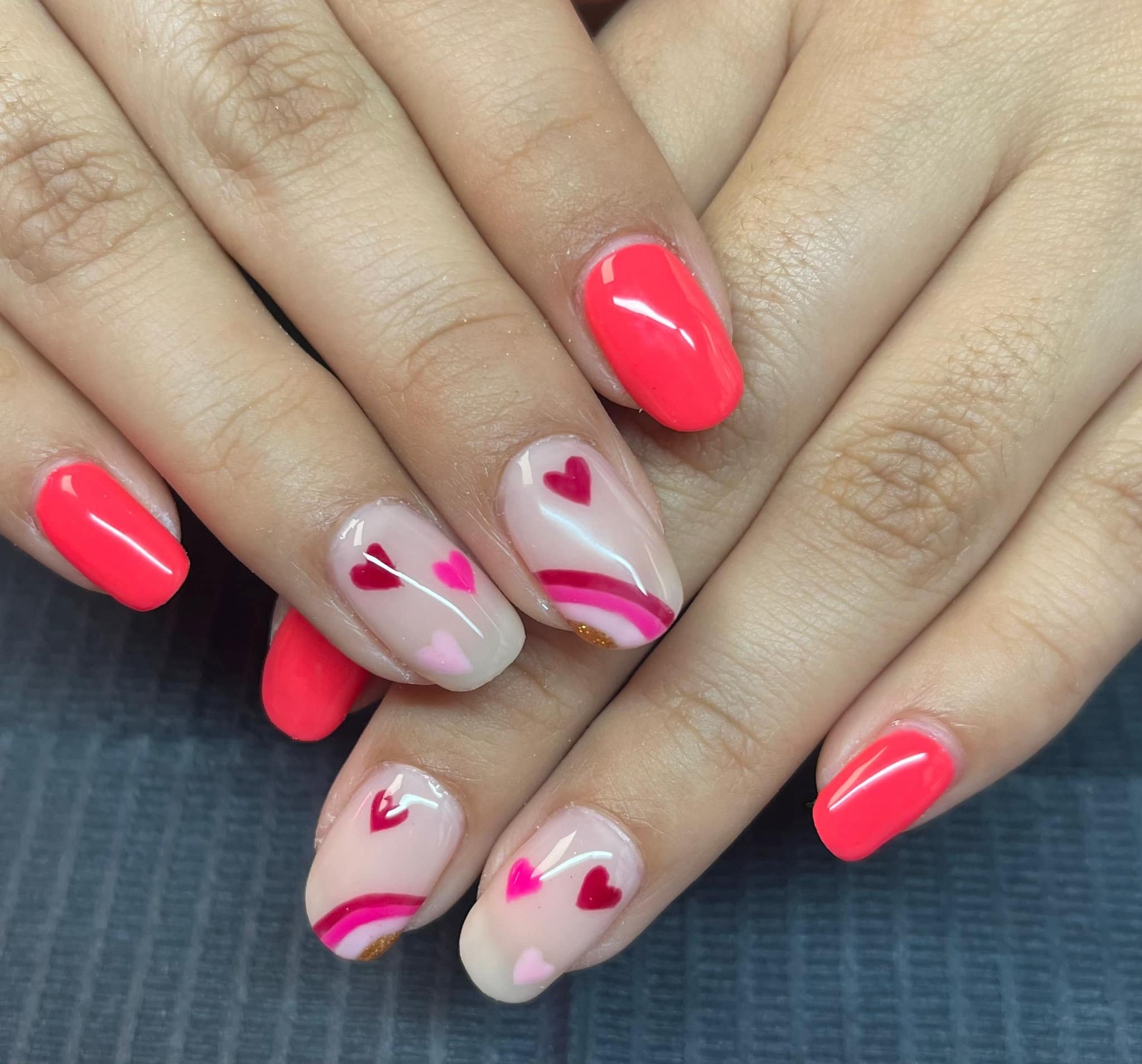 Manicure with coral-colored nails on some fingers and nails painted with a heart and stripe design in shades of pink, red, and nude on others.