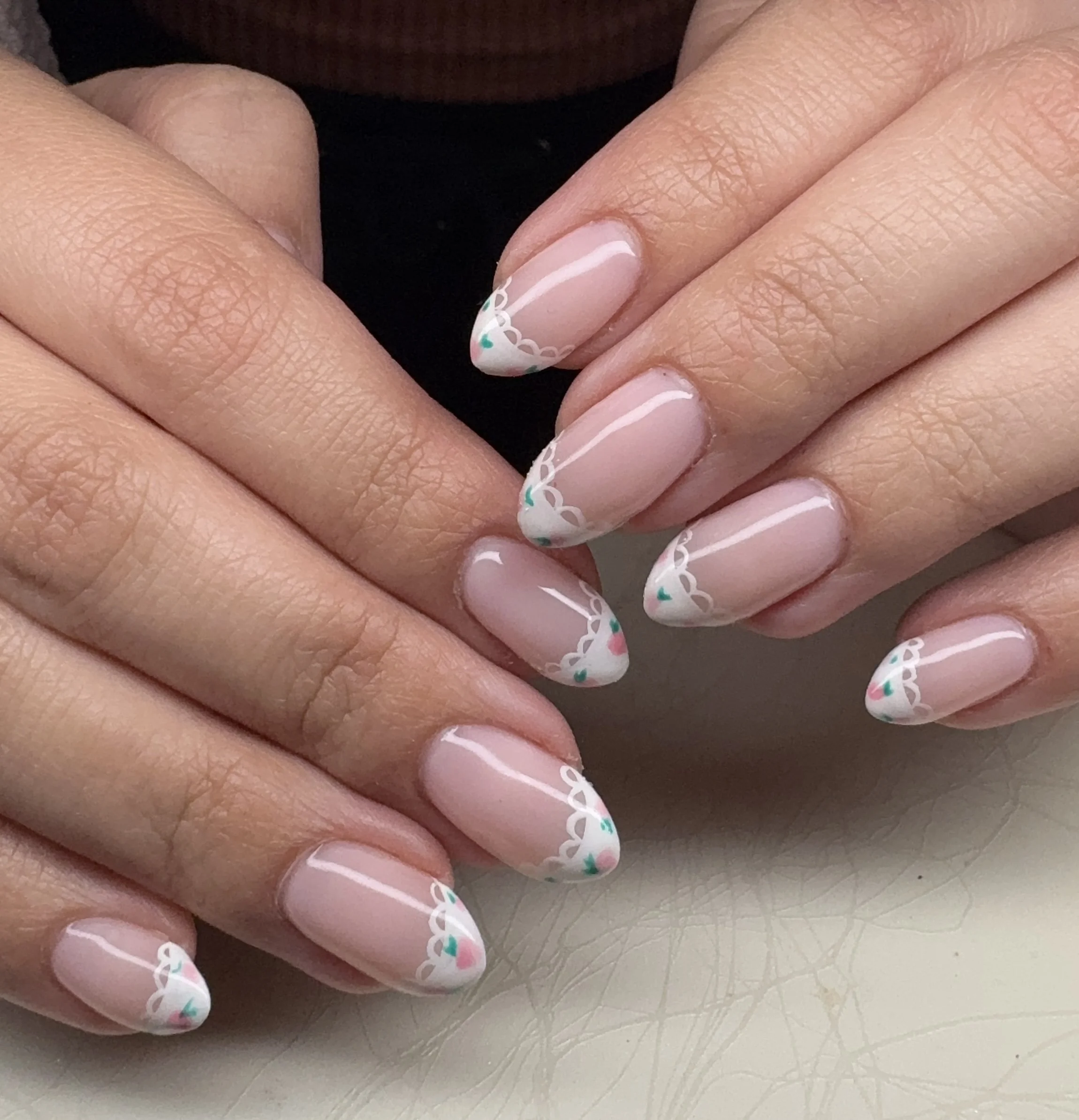 Close-up of hands with neatly manicured nails featuring pink base polish and delicate white lace-like tips with small teal and pink accents.