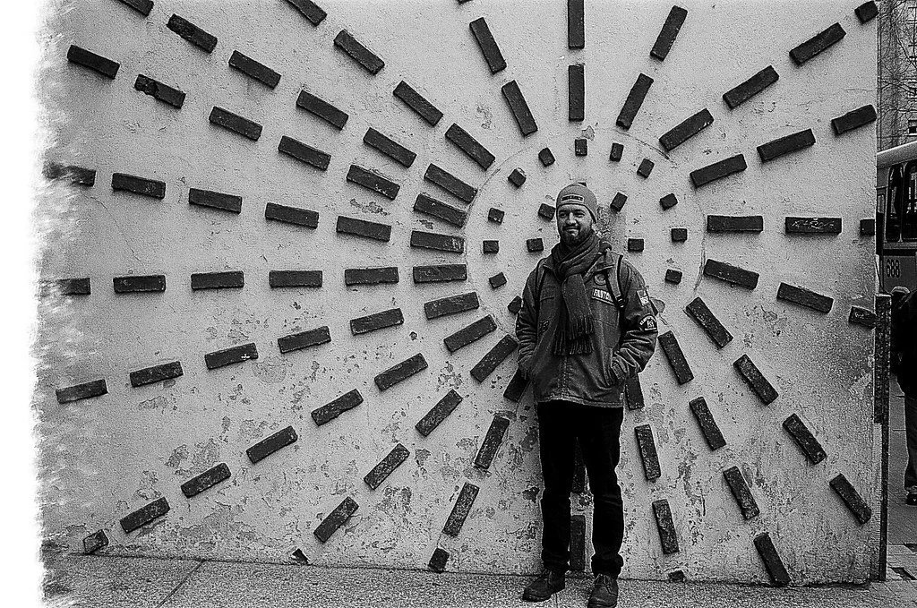 Homem sorrindo posando na frente de uma parede decorada com elementos de metal em forma de raios solares