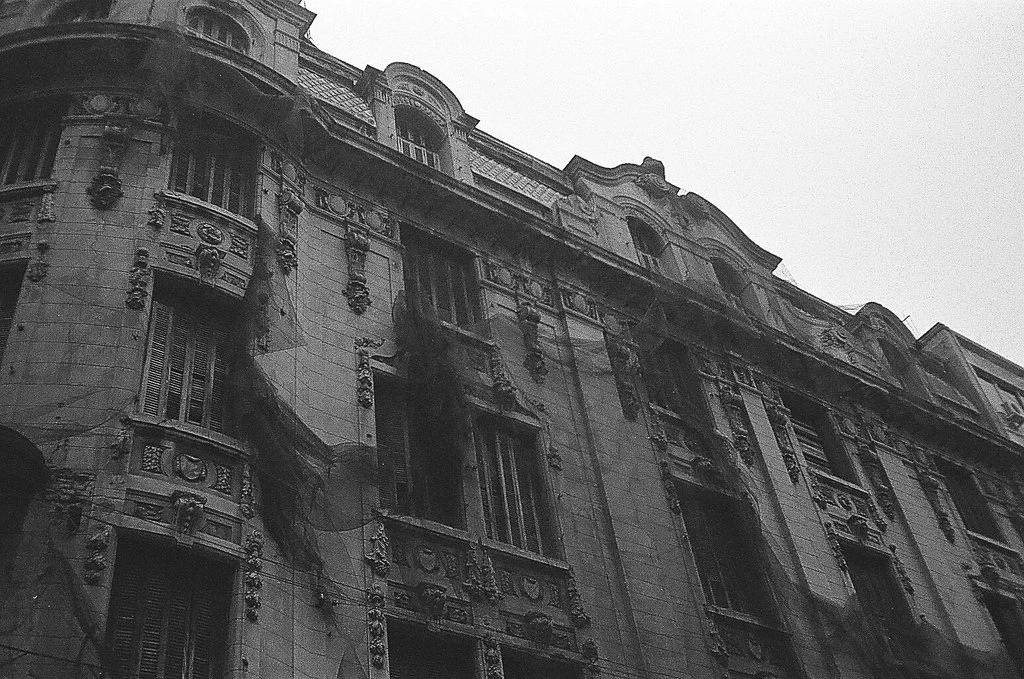 Prédio antigo com detalhes arquitetônicos ornamentados e janelas, com marcas de queimaduras e danos visíveis na fachada.
