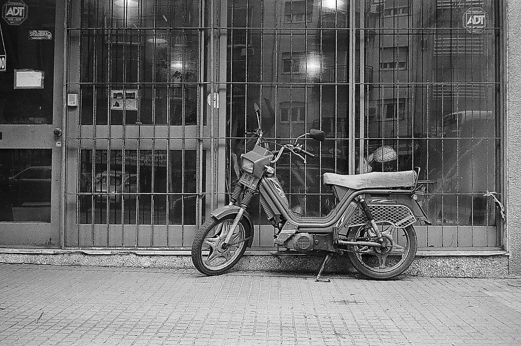 Motocicleta antiga estacionada na rua, à frente de uma loja com janelas de grades.