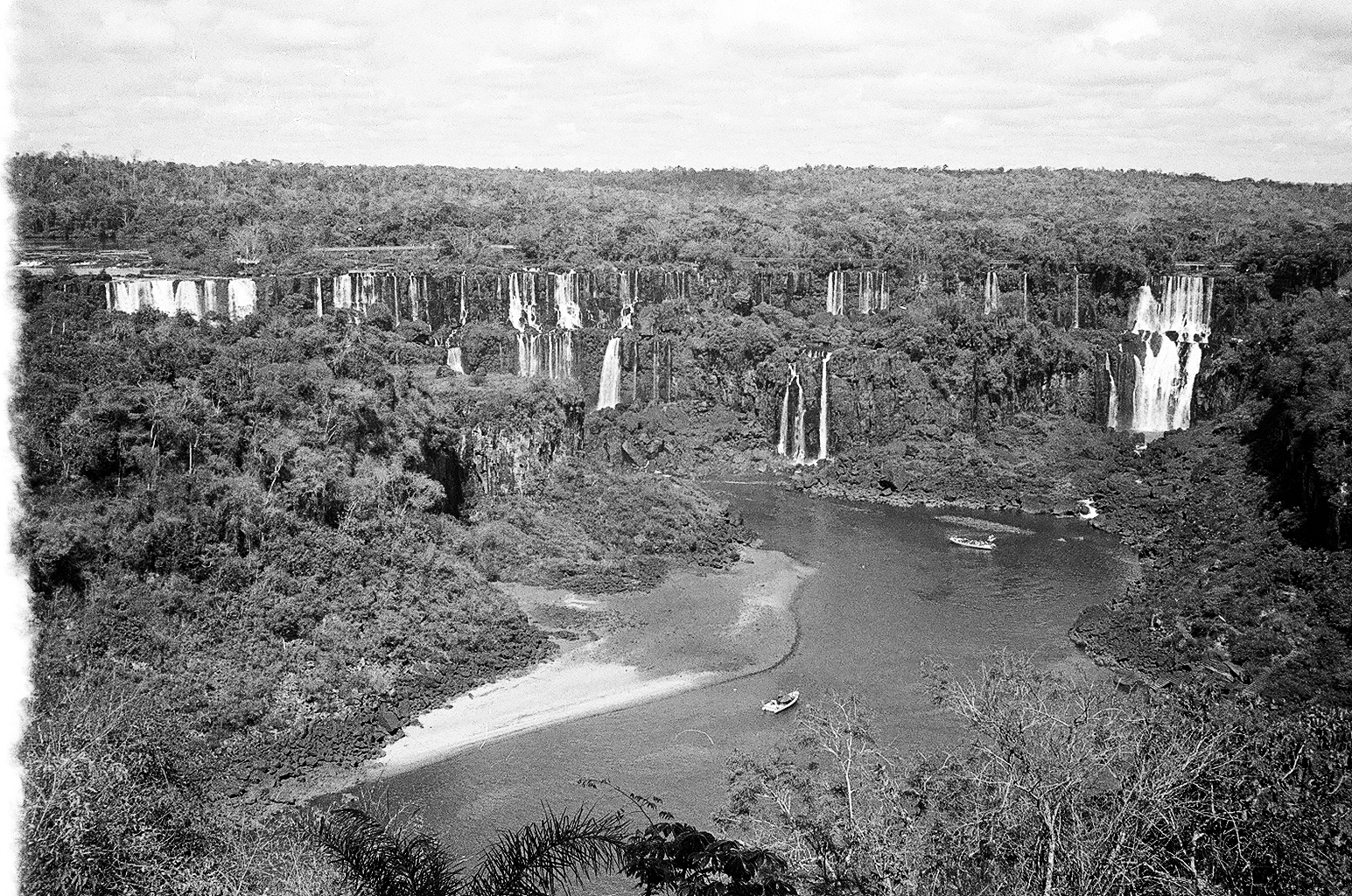 Paisagem de cachoeiras e rio cercado por vegetação densa, vista de cima em preto e branco.