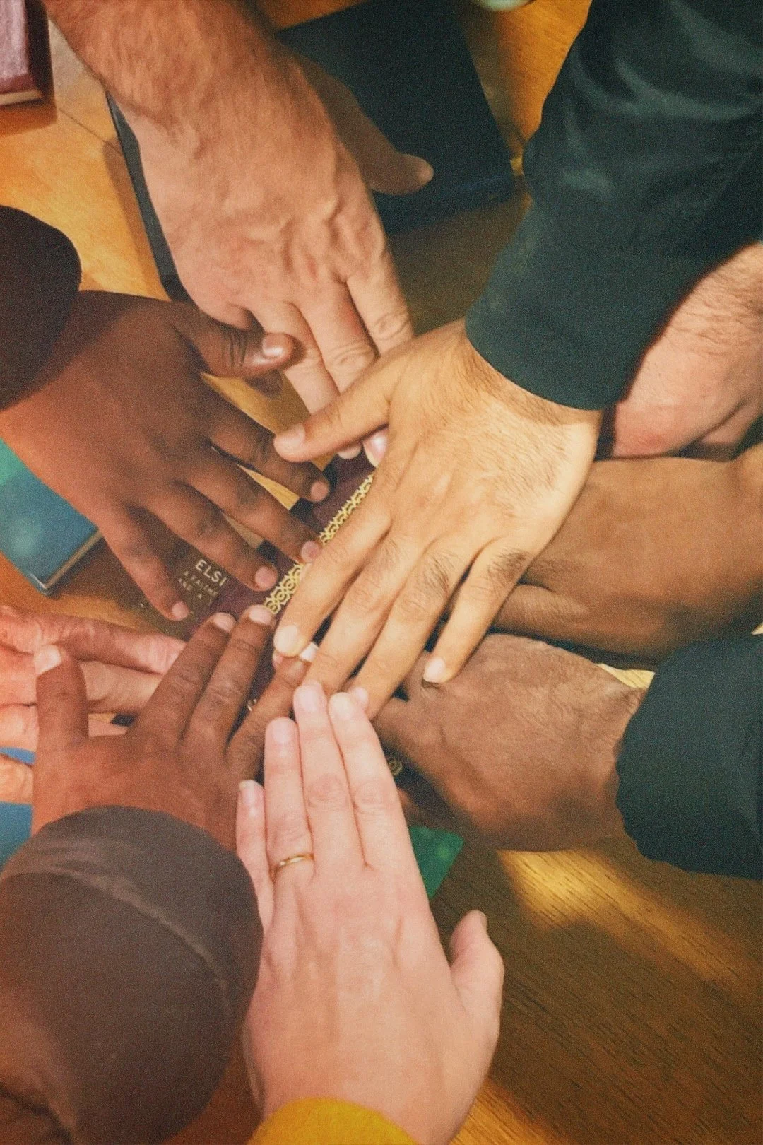 Multiple hands of different skin tones placed together in the center of a table.