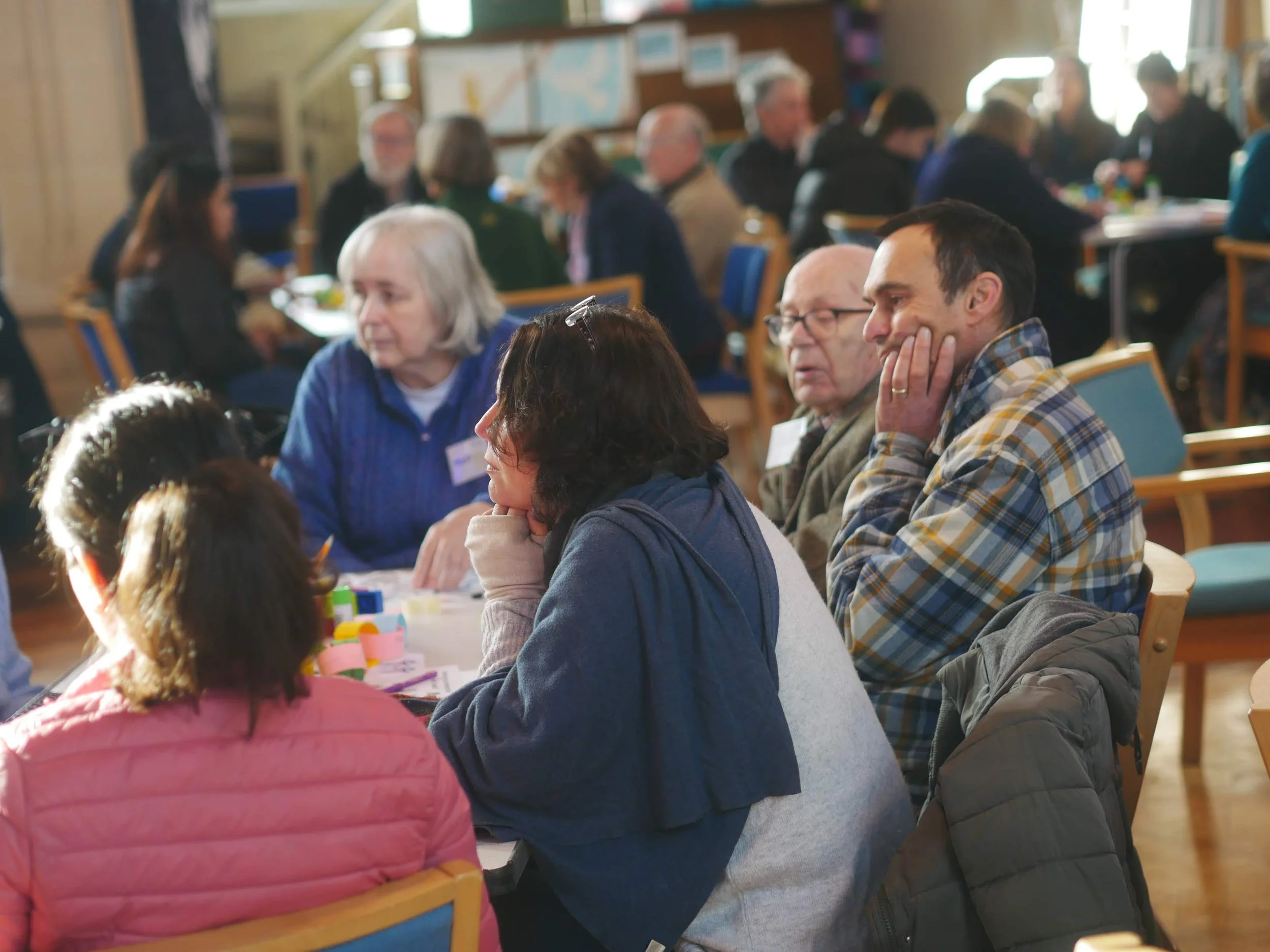 Group of people sitting at a table in a workshop or conference, engaging in conversations and activities.