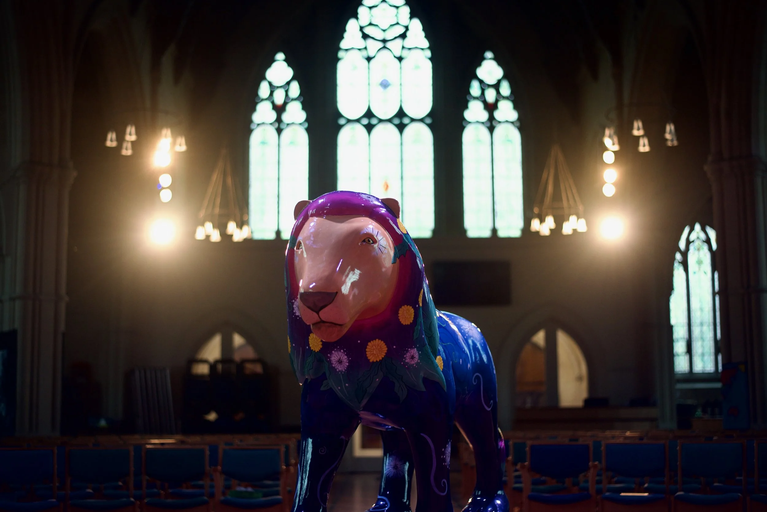 Colorful lion sculpture inside a church with stained glass windows and chandeliers.