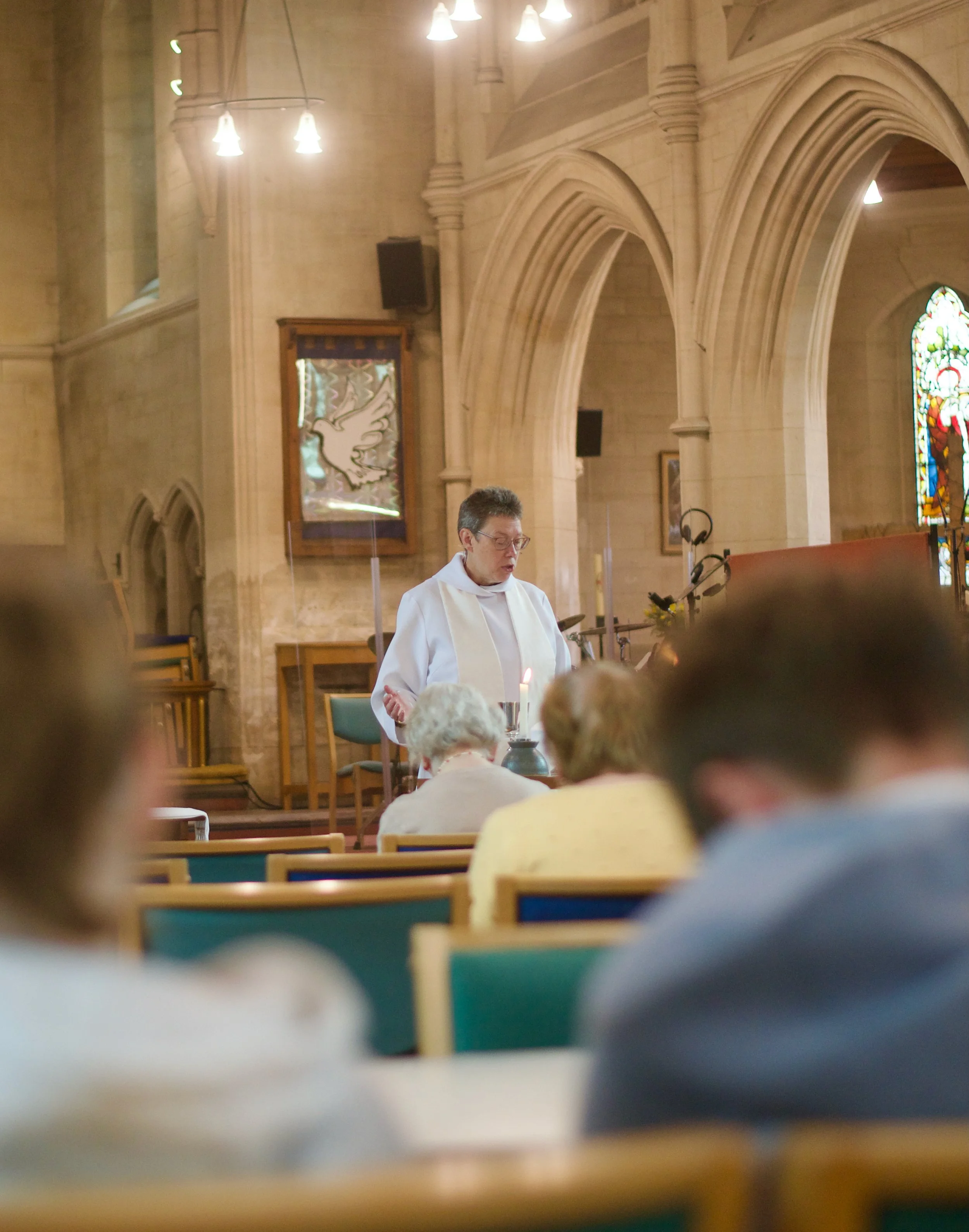 A priest conducting a church service inside a stone church with stained glass windows and arched architecture.