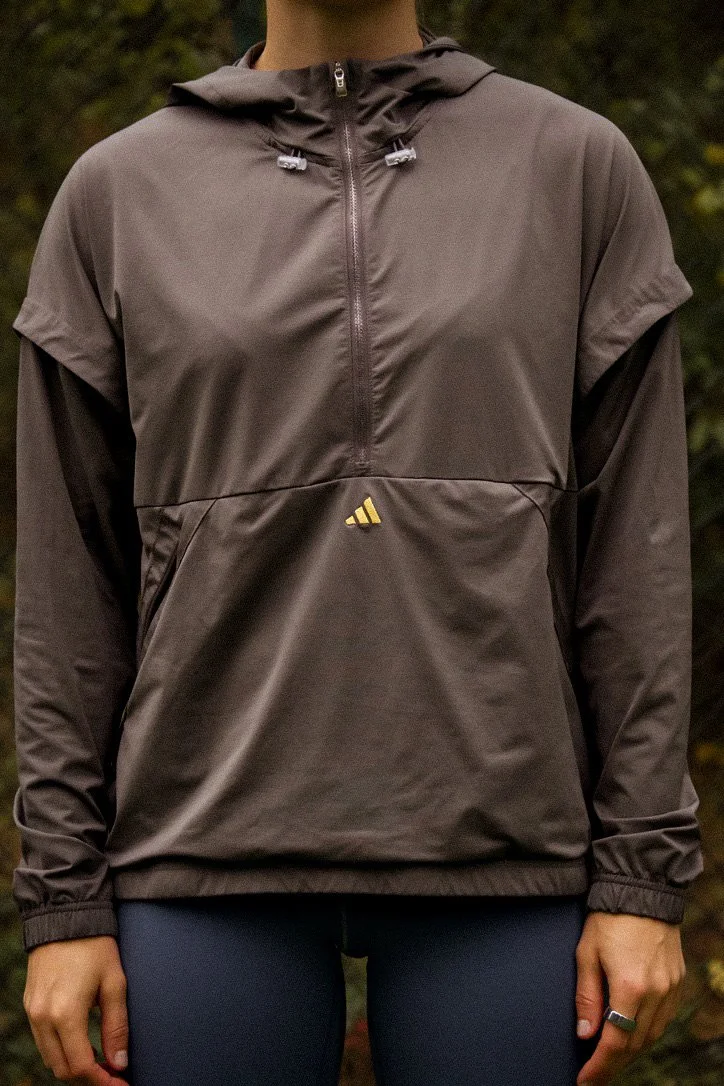 Person wearing a brown Adidas sporty windbreaker jacket with a half-zip, standing outdoors with trees in the background.