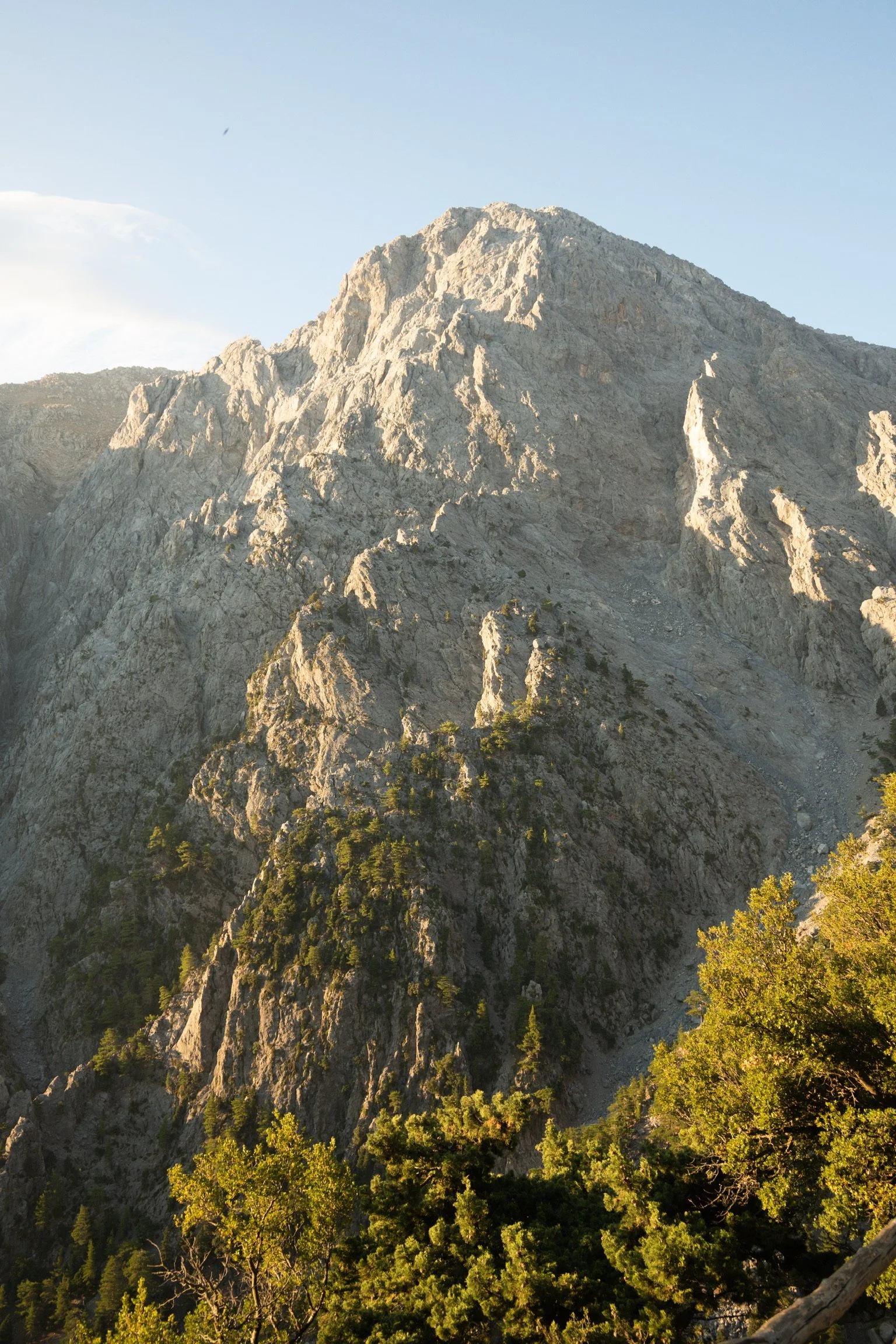 A rugged mountain with steep, rocky slopes and patches of greenery, under a clear sky.