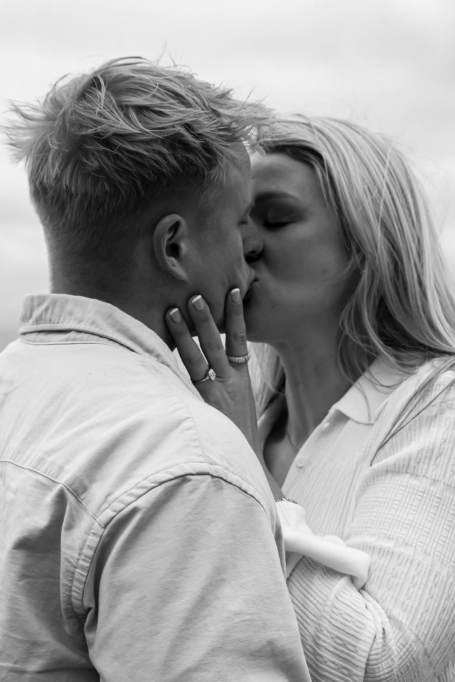 A black and white photo of a couple kissing, with the woman holding the man's face, both with eyes closed.