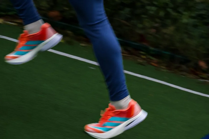 Close-up of person running on track with orange sneakers and blue and orange shoes, wearing blue jeans, on a green field with white lines.