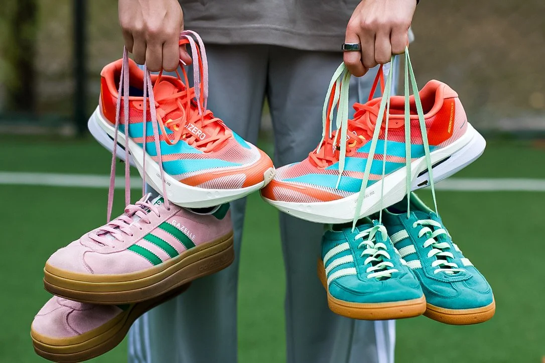 Person holding a pair of colorful running shoes and sneakers, with a grassy outdoor background.