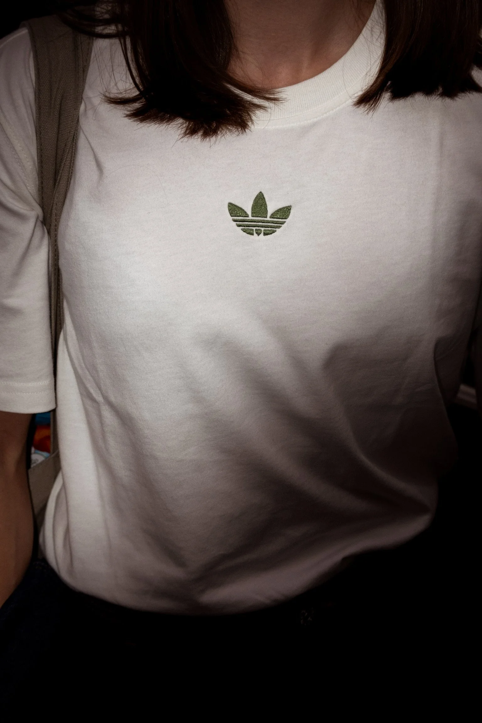 White t-shirt with a glittery Adidas trefoil logo on the chest, worn by a person with dark brown hair.
