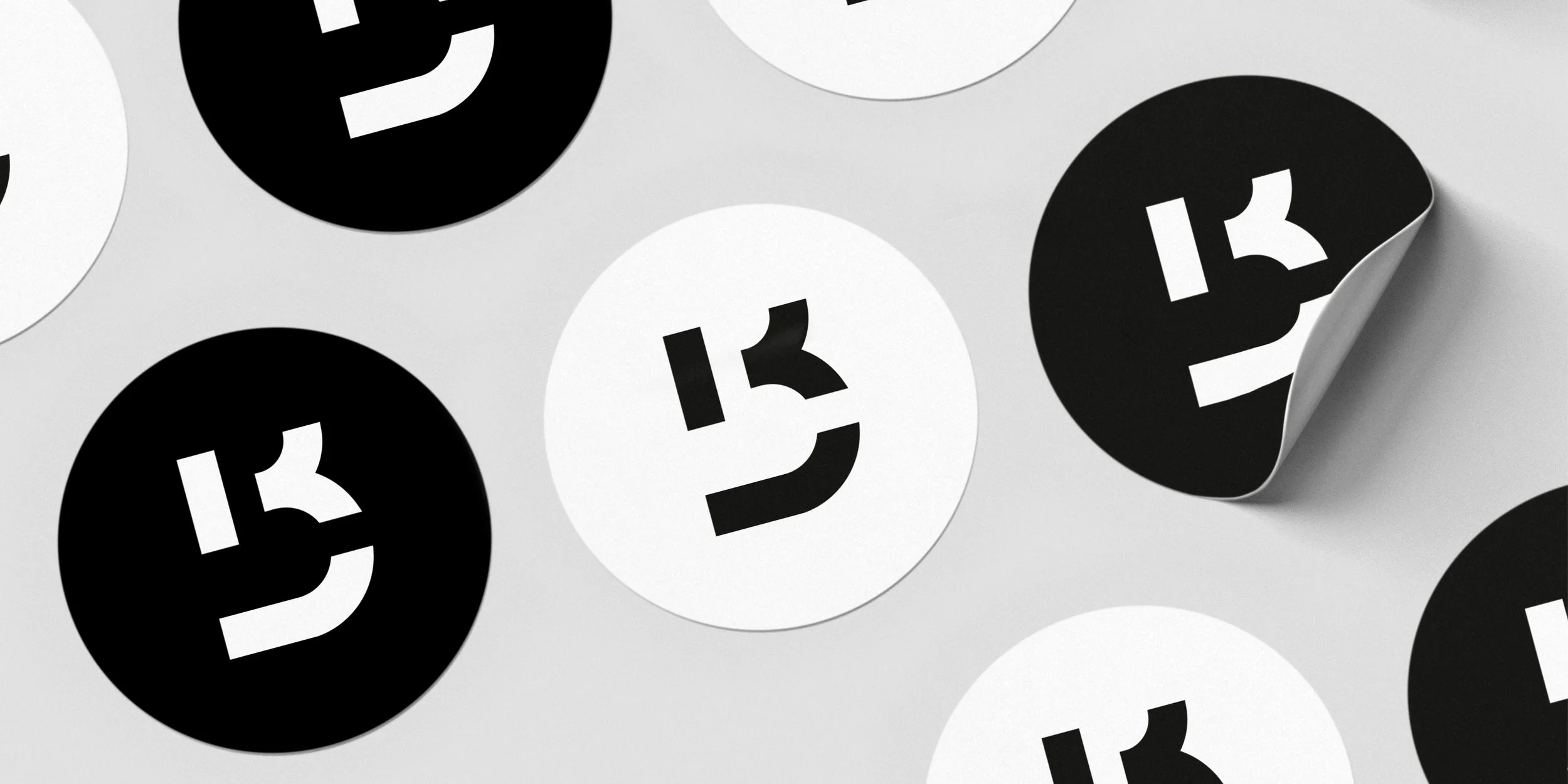 Black and white circular stickers with a stylized '13' design scattered on a light surface, one sticker partially peeling away.