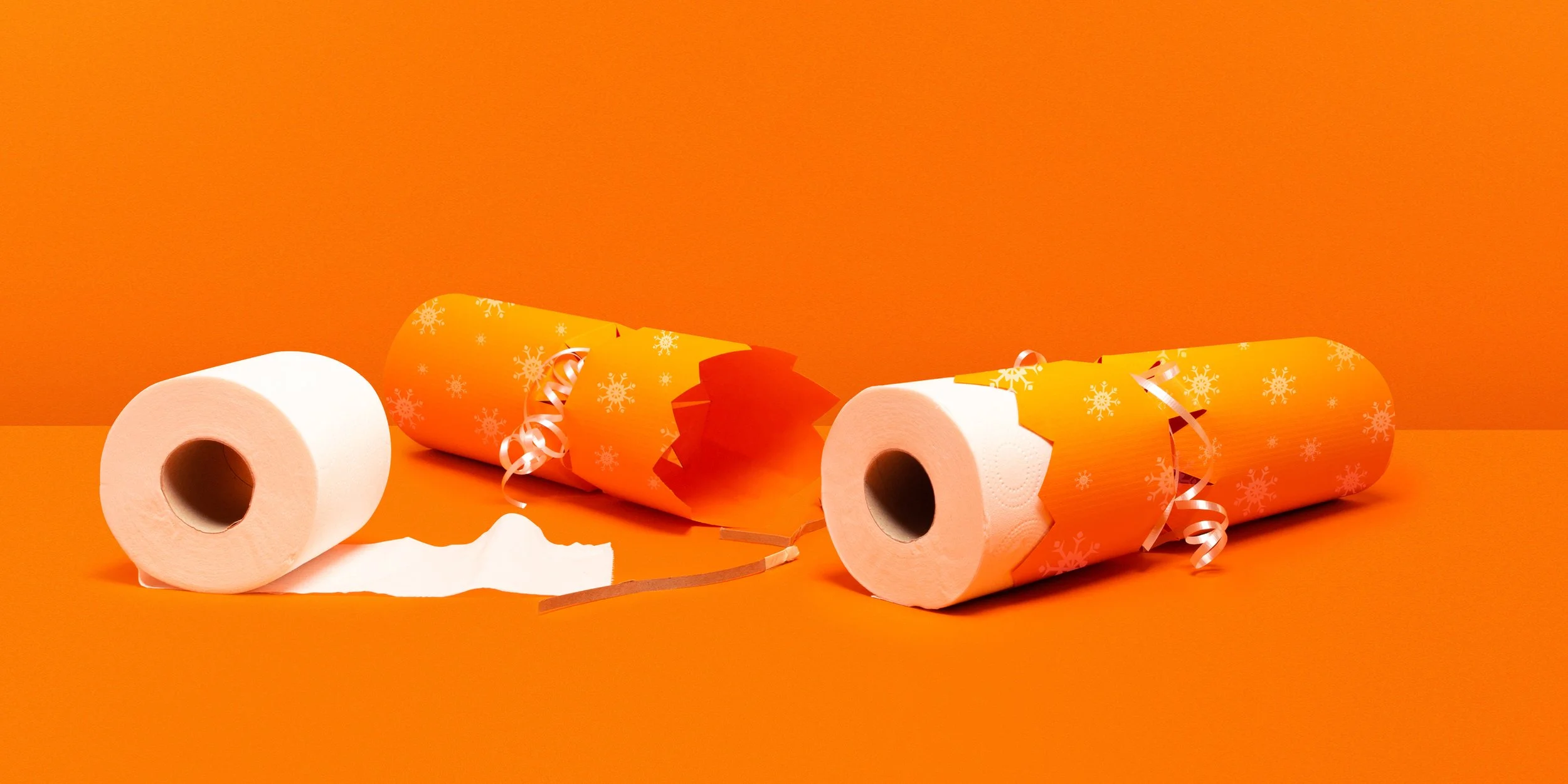 Celebratory scene with two toilet paper rolls and two orange party blowers with snowflake patterns and curled ribbons on an orange background.