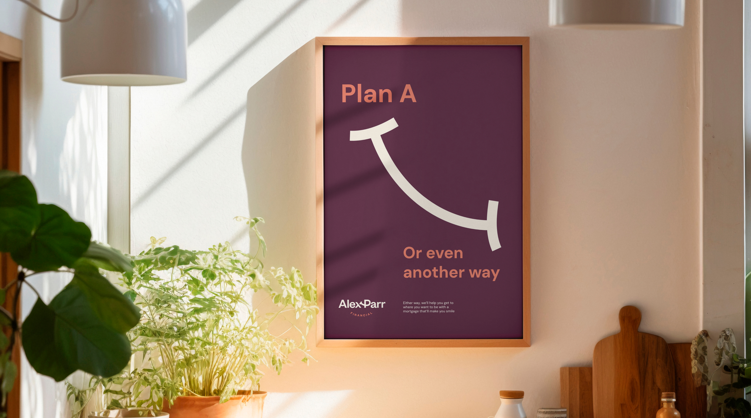 A framed sign on a wall that reads, "Plan A or even another way," with a curved arrow pointing downward. The sign is next to a white lamp, a green houseplant, and some other items on a surface, in a sunny room.