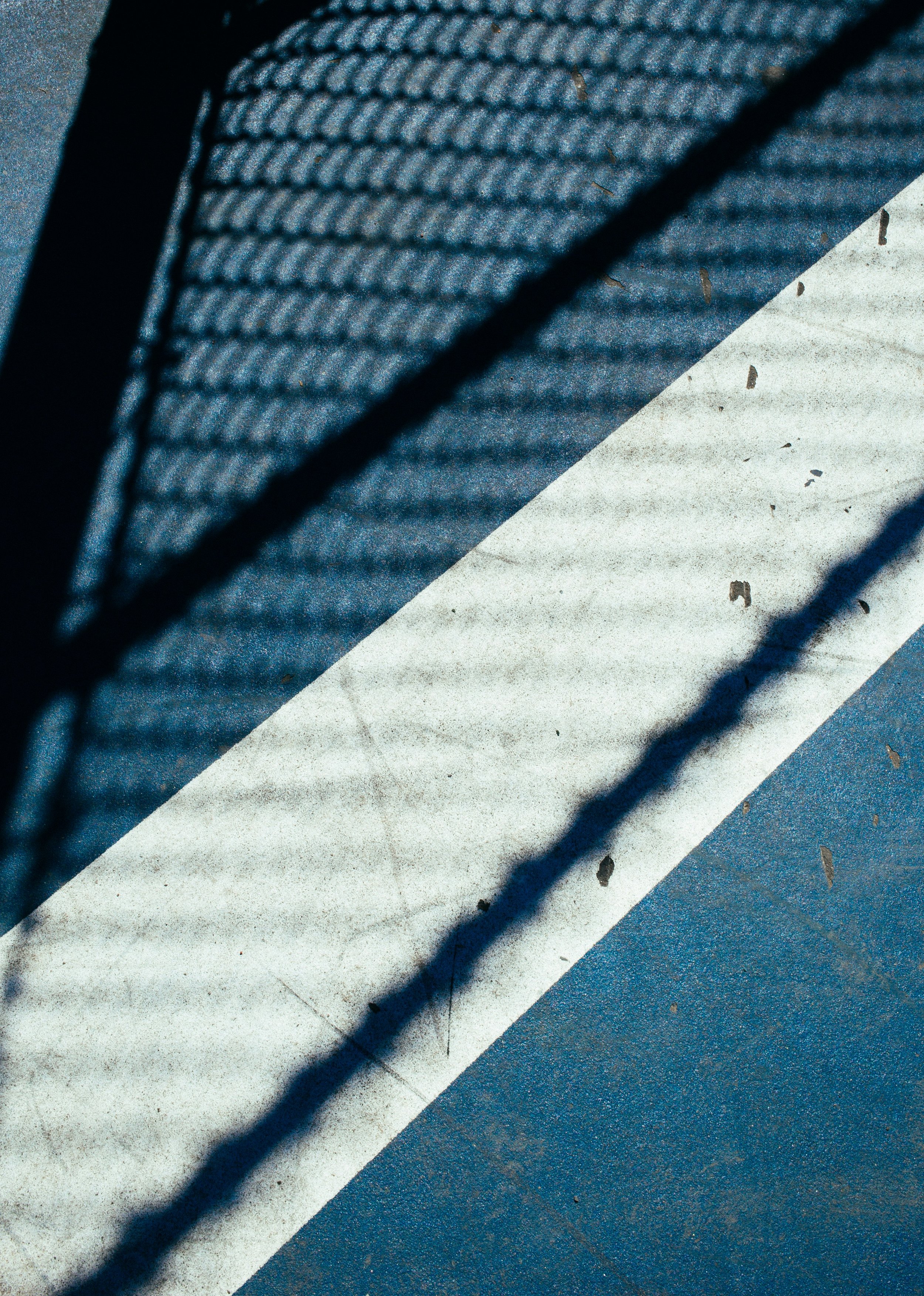Close-up of a section of a blue and white striped parking lot or sports court surface, with shadows cast across it.