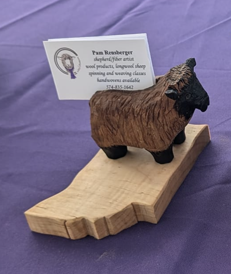 Wooden carved sheep figurine with a business card inserted behind it, on a purple surface.