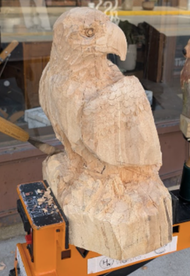 Wooden sculpture of a bird, possibly an eagle or hawk, mounted on a stand in a shop or workshop.