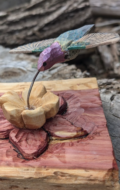 Wooden sculpture of a hummingbird hovering above a flower on a wooden base.