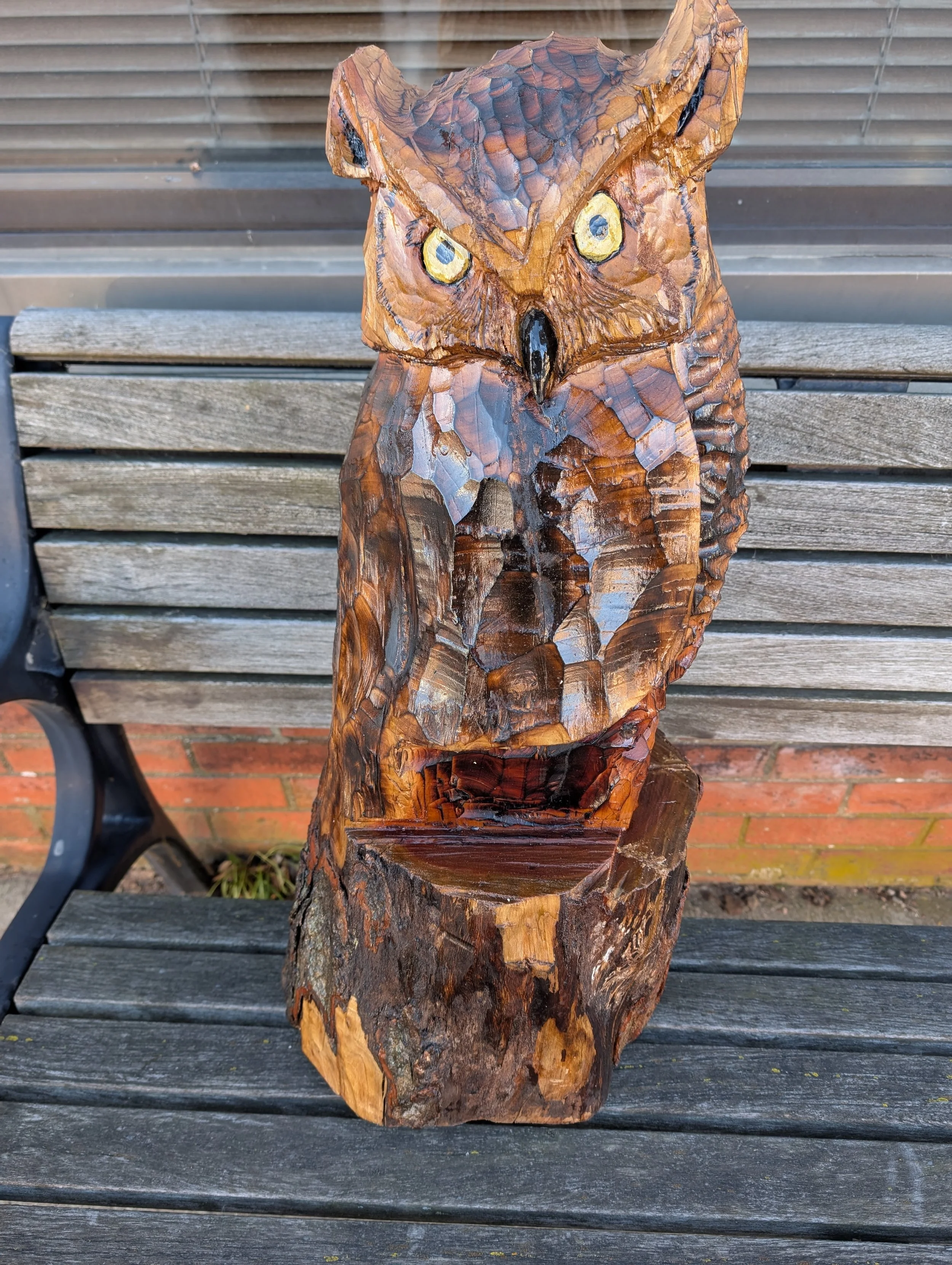 Wooden owl sculpture carved from a tree trunk, mounted on a wooden surface outdoors.