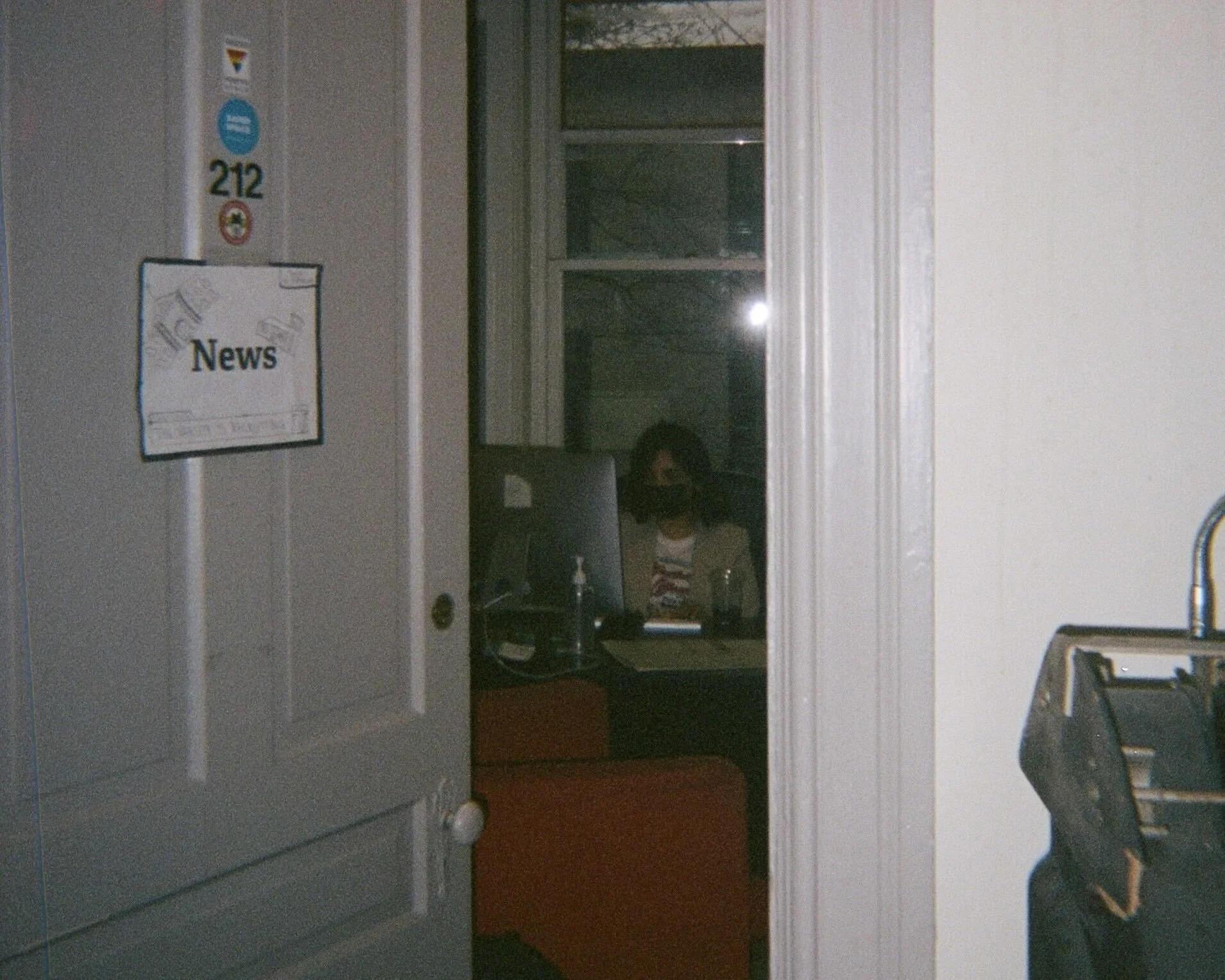 Khadija Alam working at an office computer in the evening. The door to the office has a "News" sign on it.