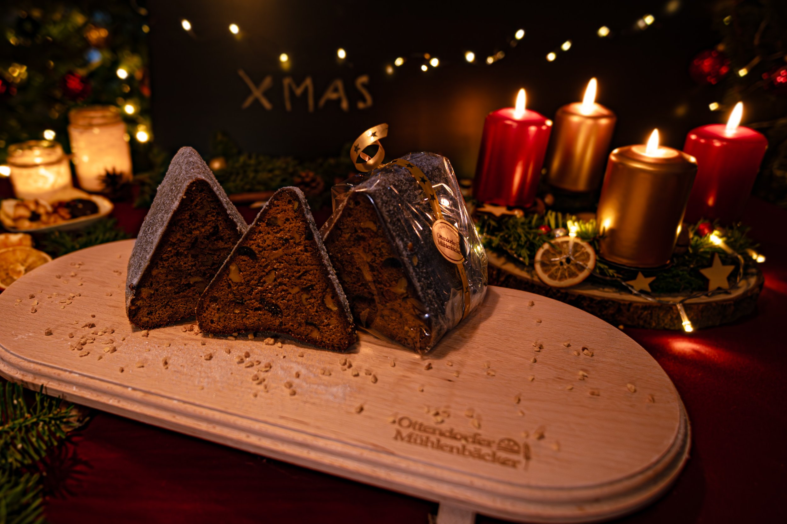 Schokoladenkuchen auf einem Holzbrett mit Weihnachtsdekoration und Kerzen im Hintergrund.