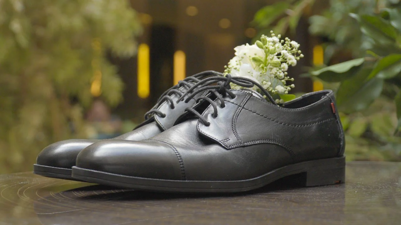 Schwarze Lederschuhe auf einem Holztisch mit Blumen im Hintergrund