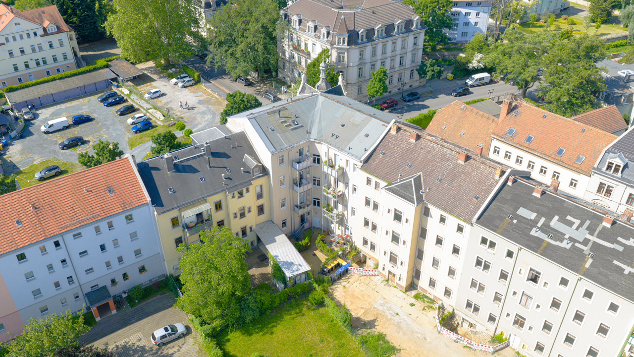 Luftaufnahme eines Wohnblocks mit einem Innenhof, umgeben von mehreren Mehrfamilienhäusern, Bäumen und einem Parkplatz.