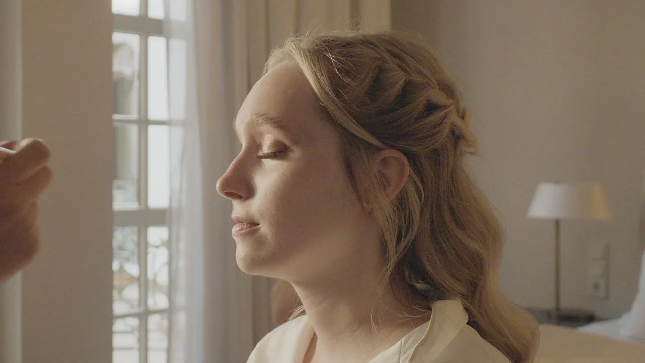 Eine Frau sitzt mit geschlossenen Augen in einem hell erleuchteten Raum, im Hintergrund eine Stehlampe und ein Fenster mit weißen Vorhängen.