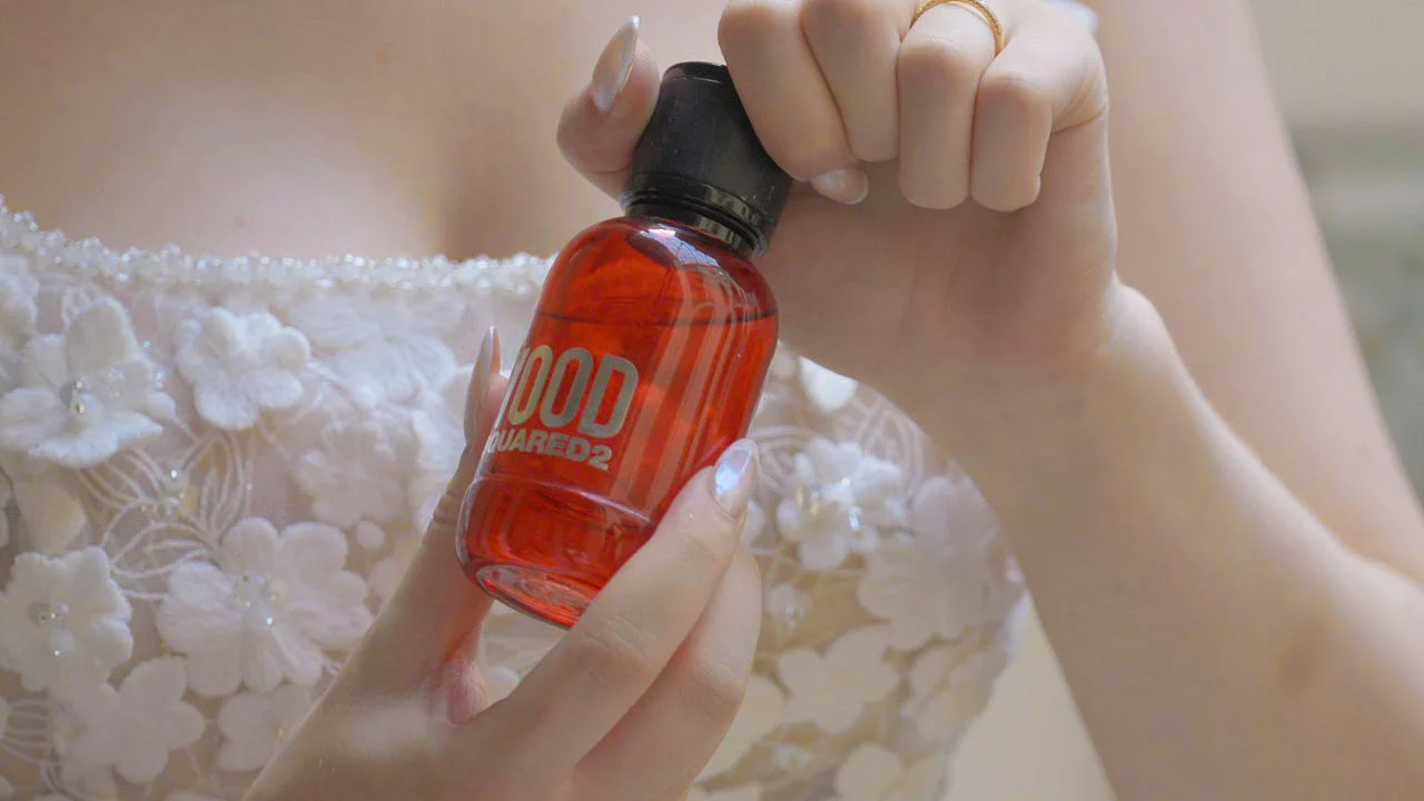 Hand hält eine rote Flasche mit dem Label 'FOOD' und 'DSQUARED2', während eine andere Hand die Flasche schräg hält.