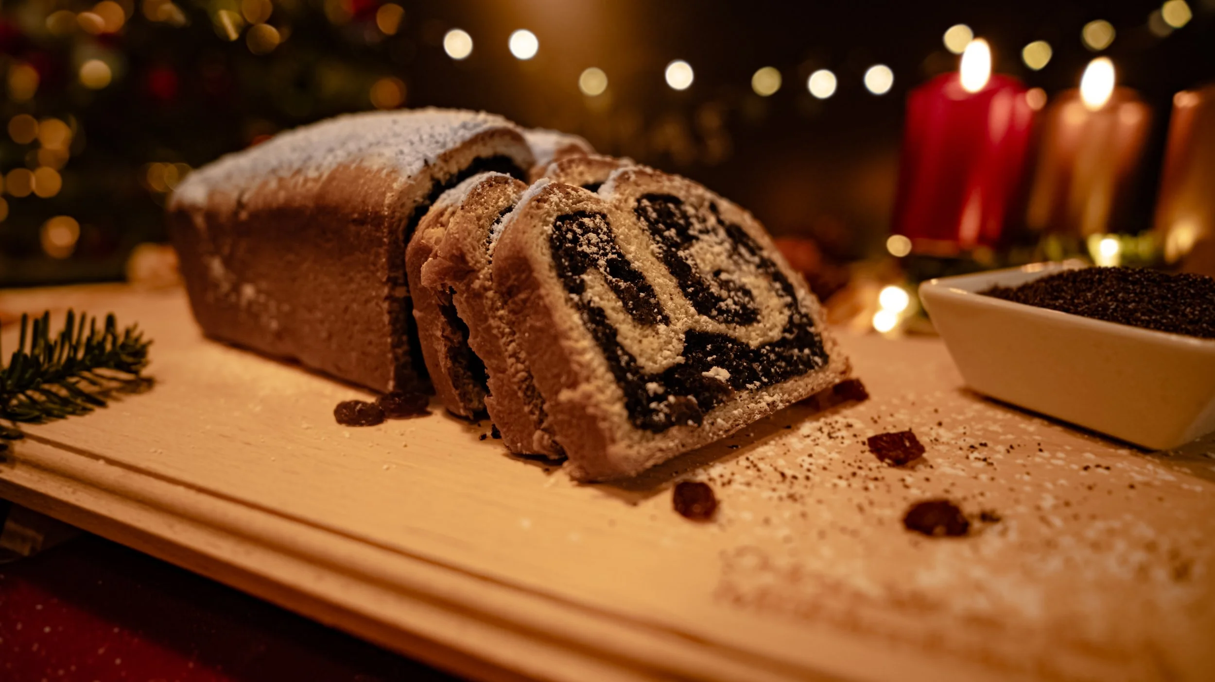 Ein Schneckenkuchen mit Zuckerguss auf einem Holzteller, umgeben von Zimtsternen und Weihnachtsdekoration, im Hintergrund brennen Kerzen.