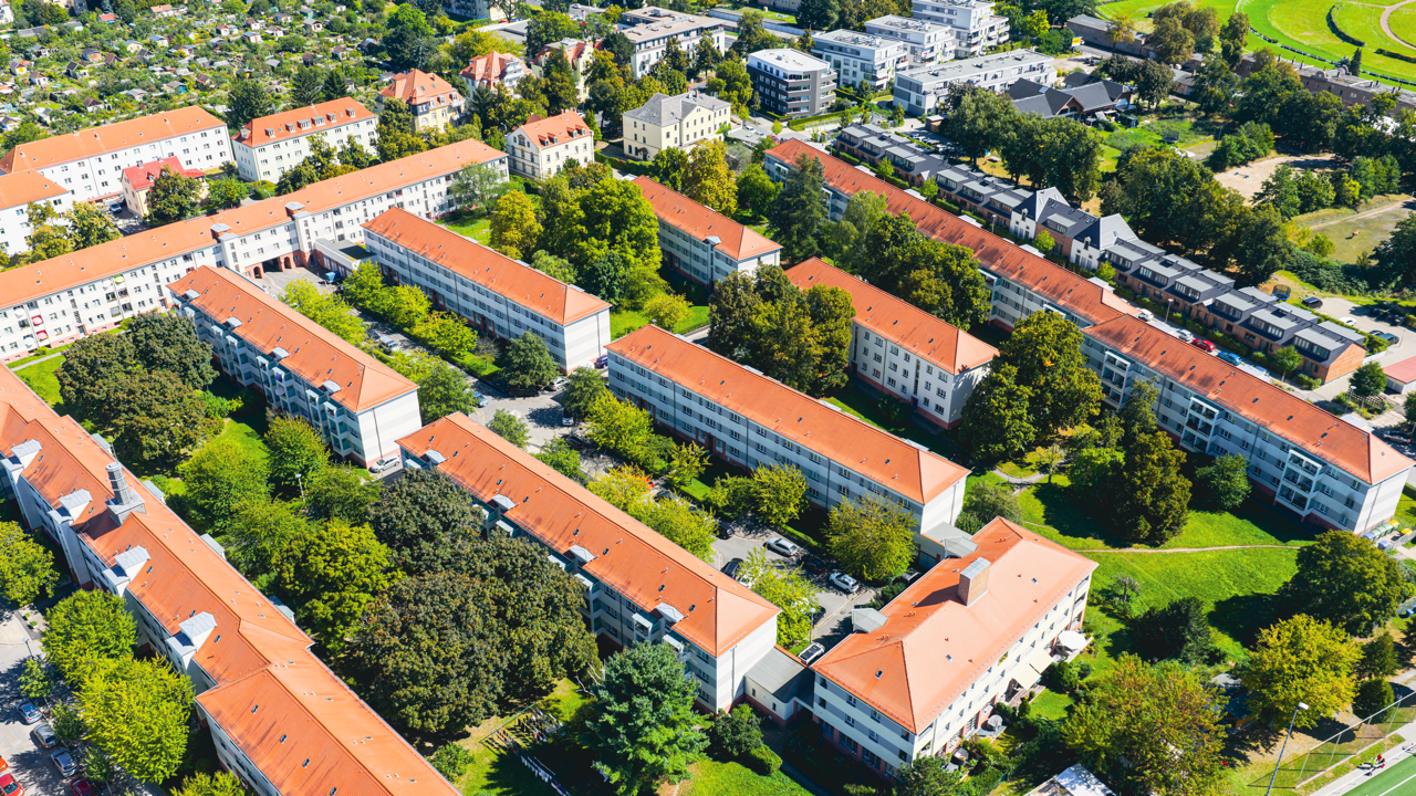 Luftaufnahme eines Wohnviertels mit mehrstöckigen weißen Gebäuden mit roten Dächern, grünen Bäumen und Straßen in einer Stadt.