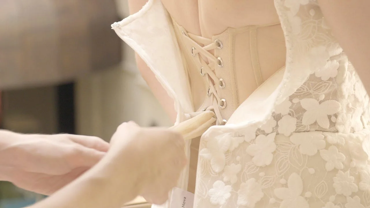 Jemand zieht das Kleid einer Braut an, das weiß mit floralem Muster ist.