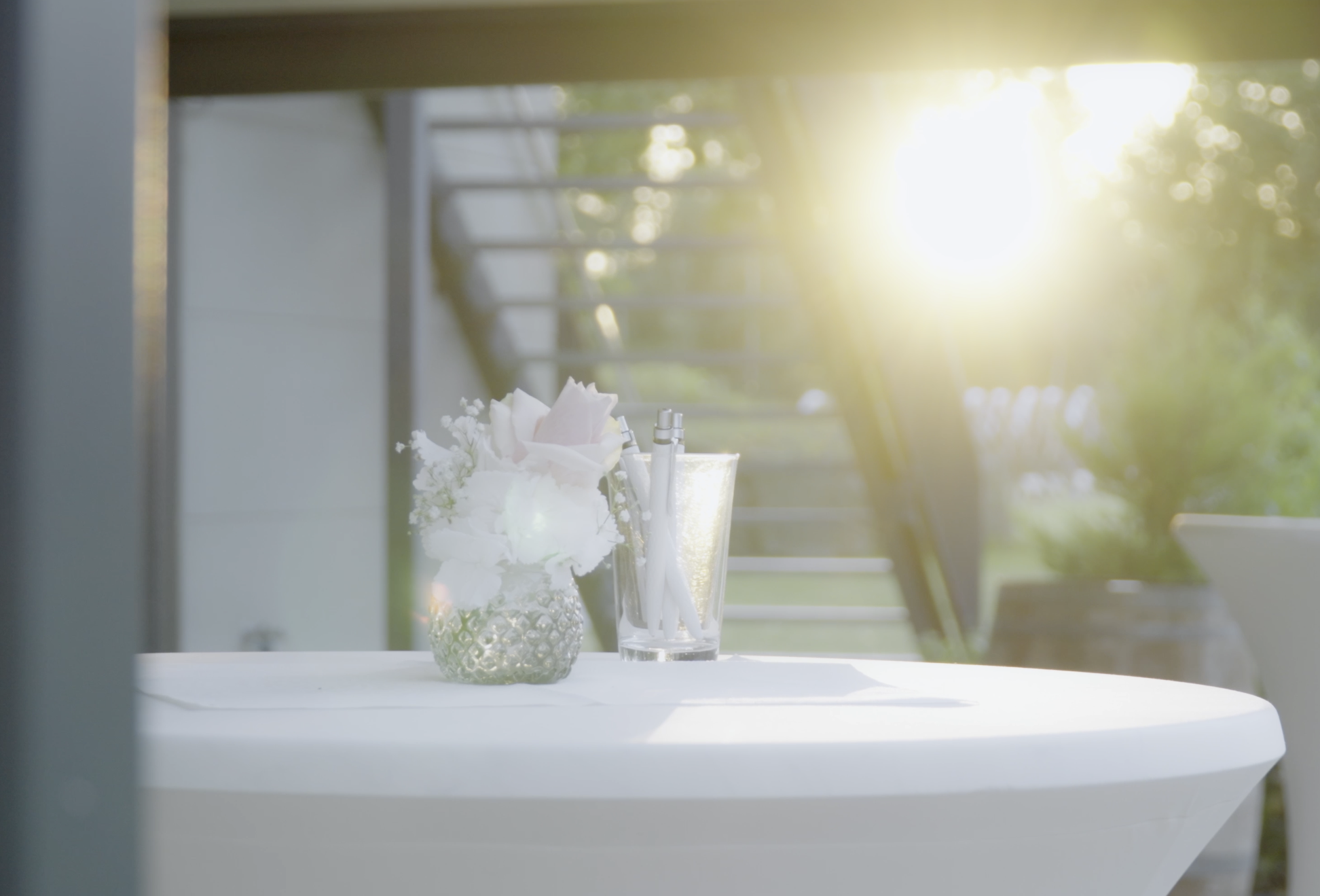 Blumen und Schreibutensilien auf einem weißen Tisch im Freien bei Sonnenuntergang.