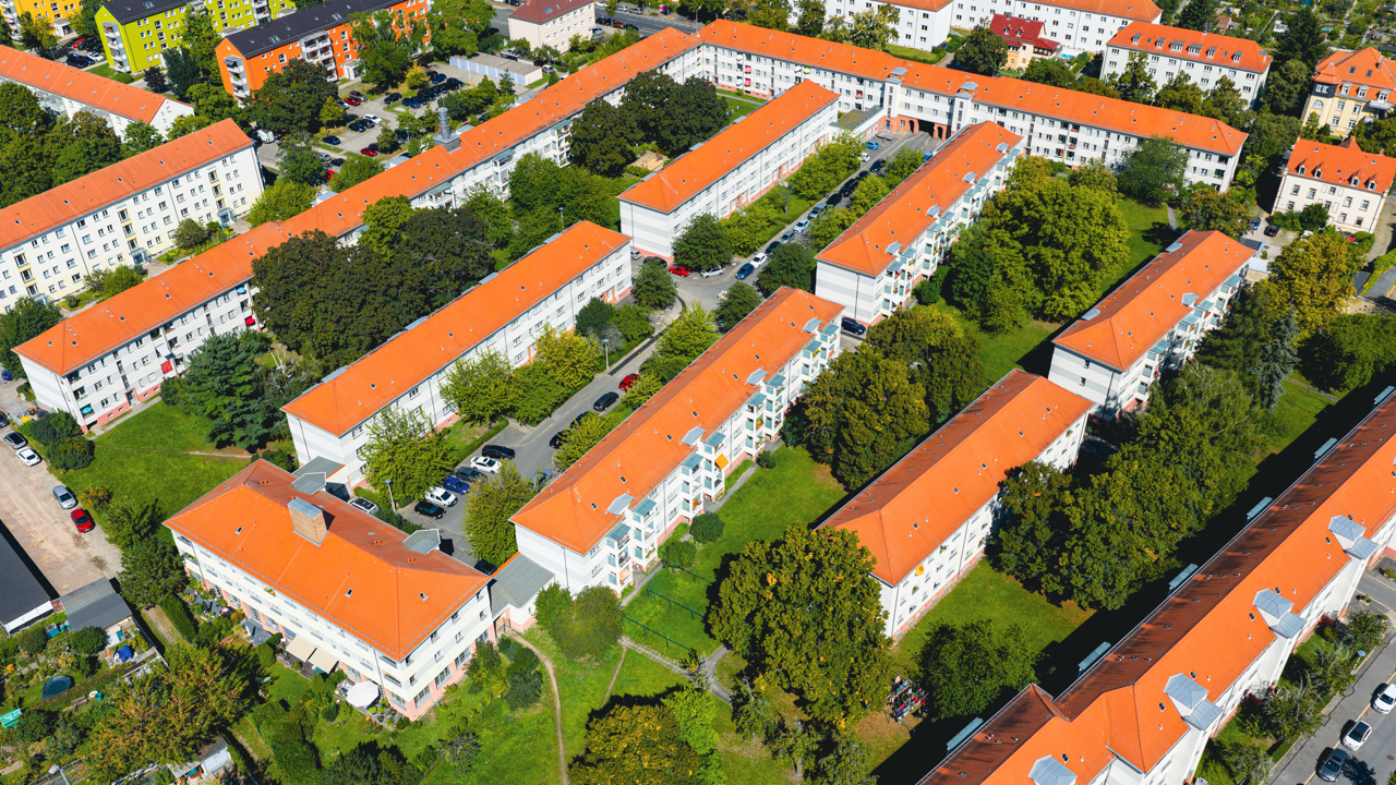 Luftaufnahme eines Wohnviertels mit mehreren weißen Mehrfamilienhäusern mit roten Dächern, umgeben von Grünflächen und Bäumen, in einer Stadt.