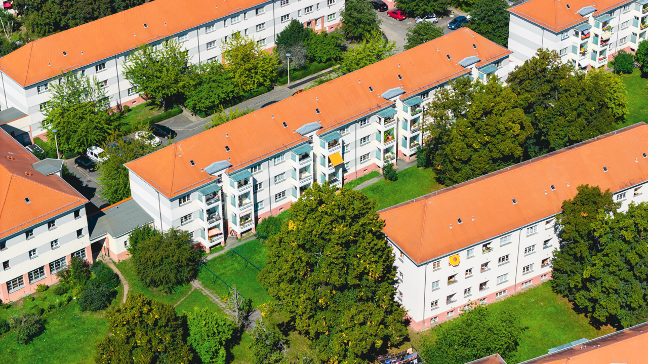 Luftaufnahme mehrerer mehrstöckiger Wohngebäude mit roten Dächern, umgeben von Bäumen und grünem Rasen, in einer gepflegten Wohnsiedlung in Deutschland.