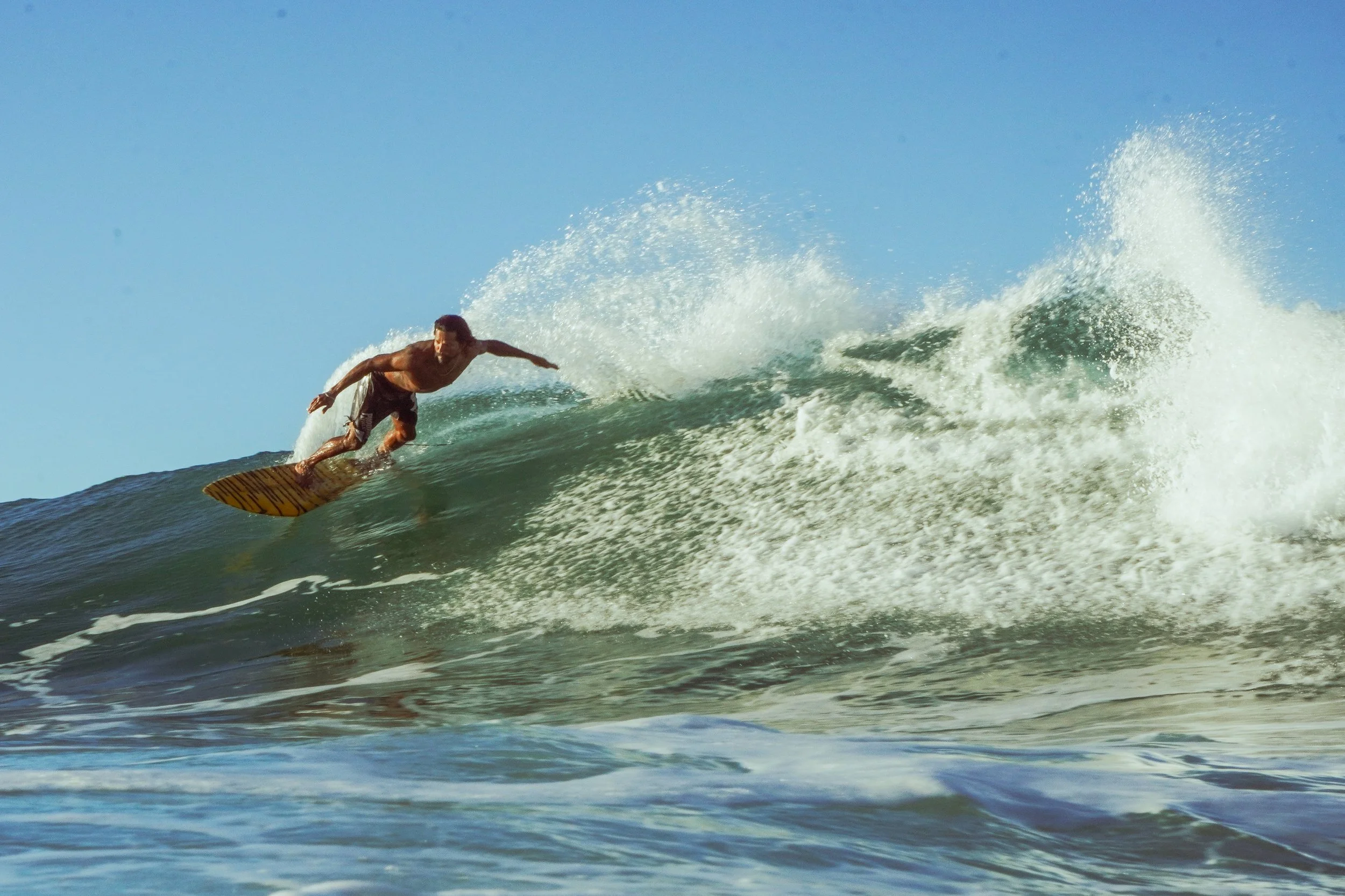 Male surfer riding a wave on a sunny day.